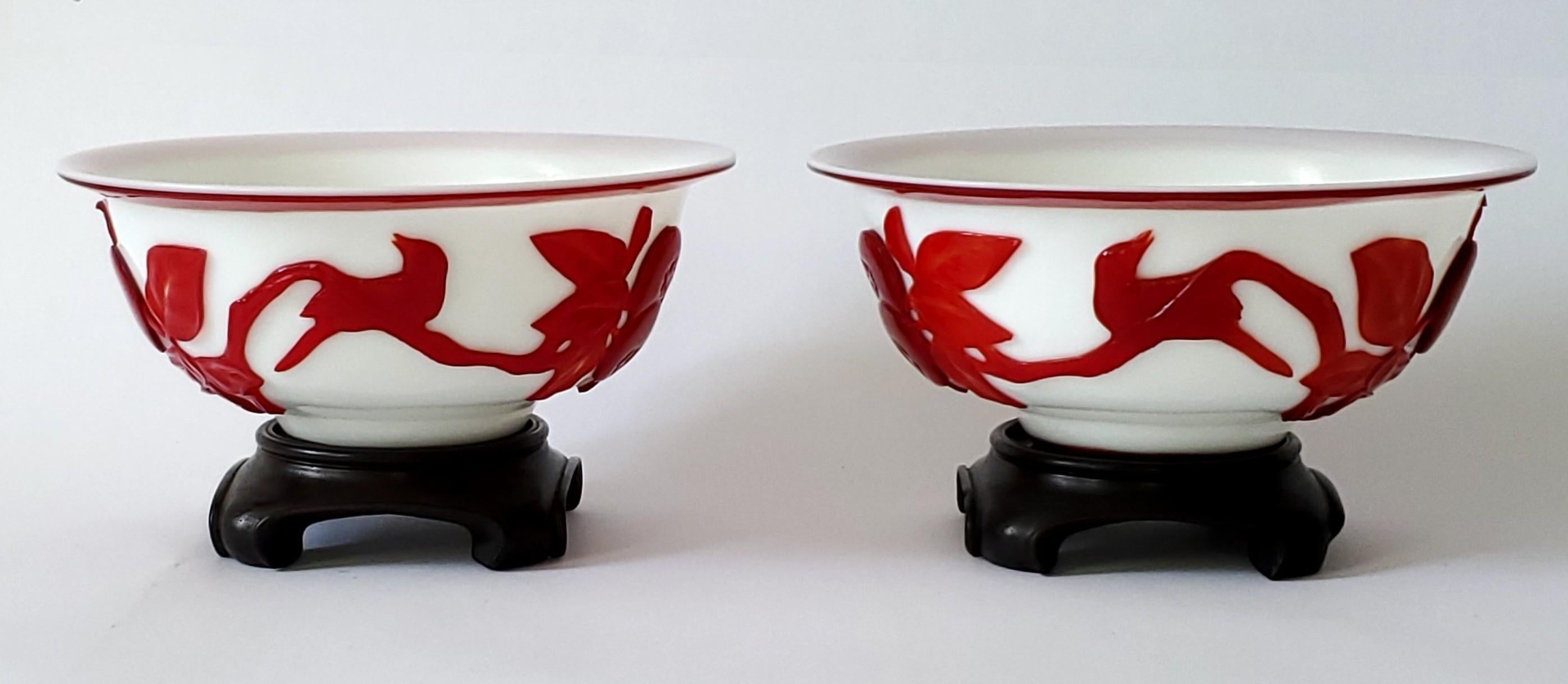 Offrant une paire de bols en verre de Pékin avec leurs supports d'origine, vers les années 1940. Ces jolis bols en verre blanc translucide, ornés de motifs rouges sculptés, datent de la période de la République chinoise. 

Les dessins comprennent