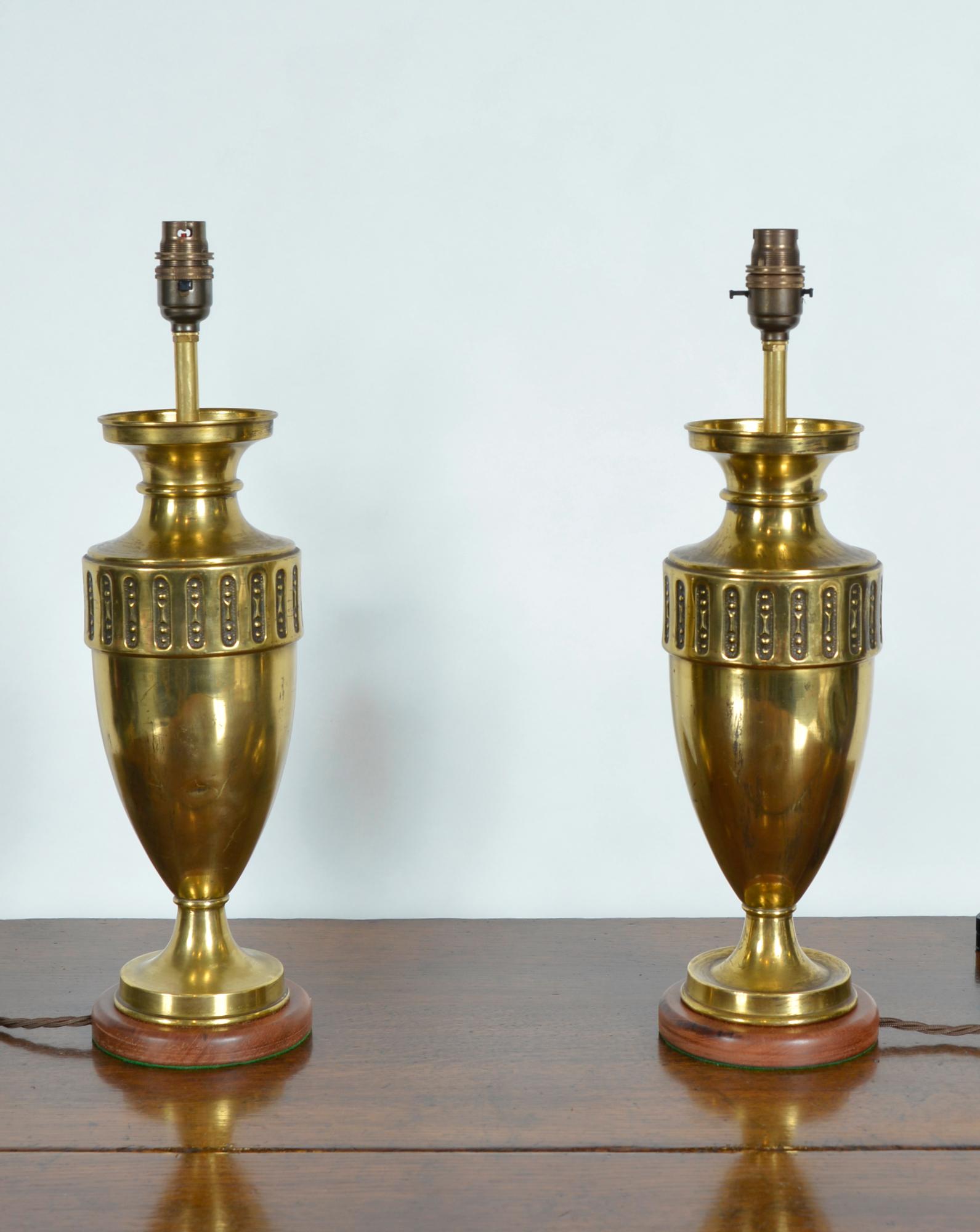 A stylish pair of early 20th century Continental brass urn shaped vases in the Art Nouveau style. These have at some time been converted into a pair of table lamps. Each urn is mounted on a wooden base with a green baize scratch preventer. There is