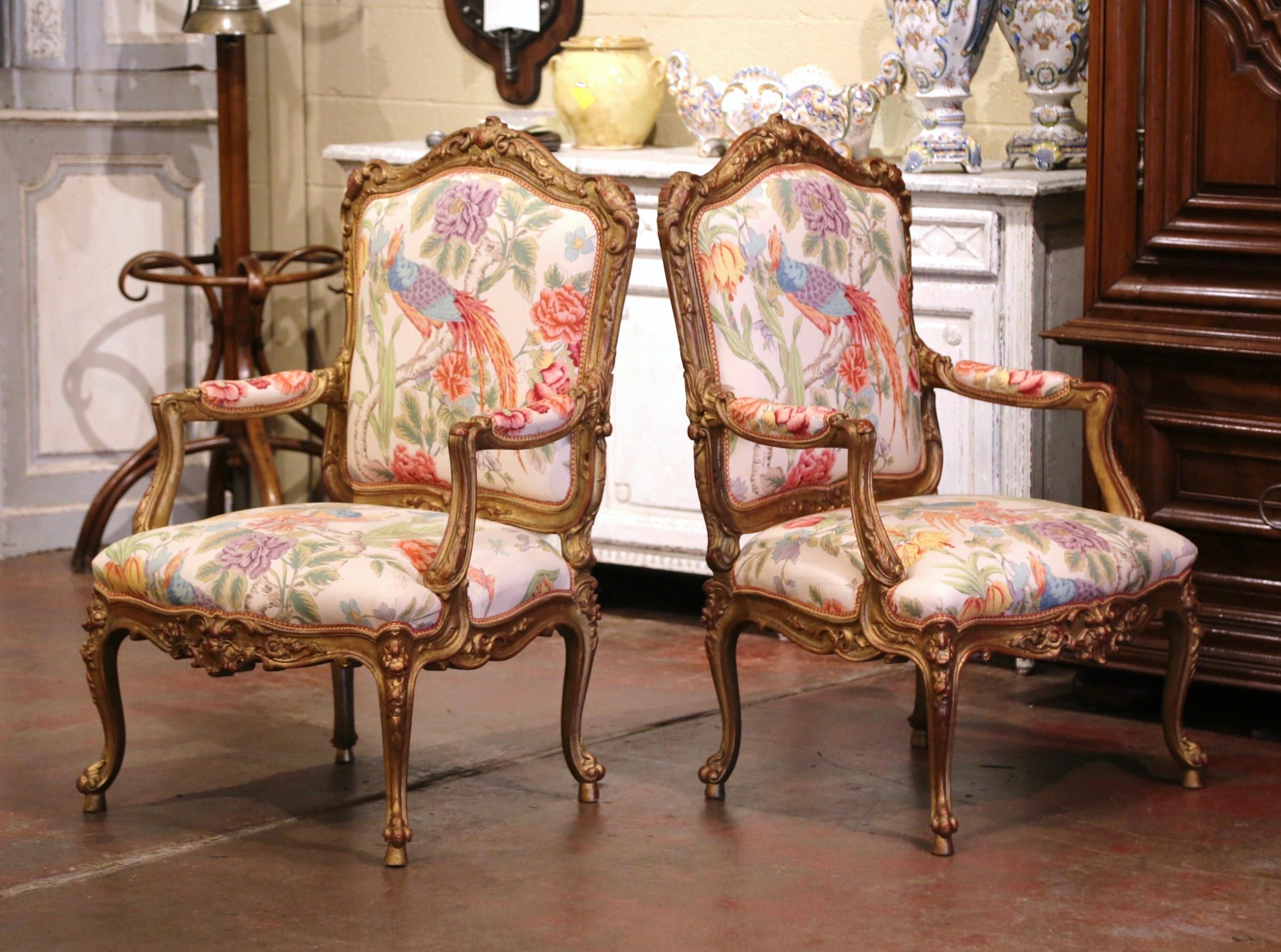 Crafted in France circa 1920, each antique armchair stands on cabriole legs decorated with floral and leaf motifs at the shoulder, and ending with escargot feet. The arched back is decorated with shell and foliage motifs, and embellished with