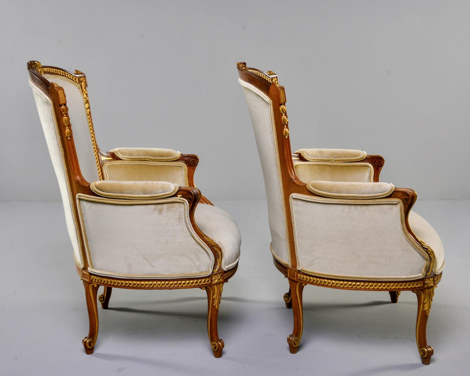 Pair of Louis XV style French armchairs feature beautifully carved and gilded walnut frames, circa 1900. Tall seat backs have carved crests and gilt detail, padded arms and scrolled cabriole legs. Newly upholstered in a golden wheat colored velvet.