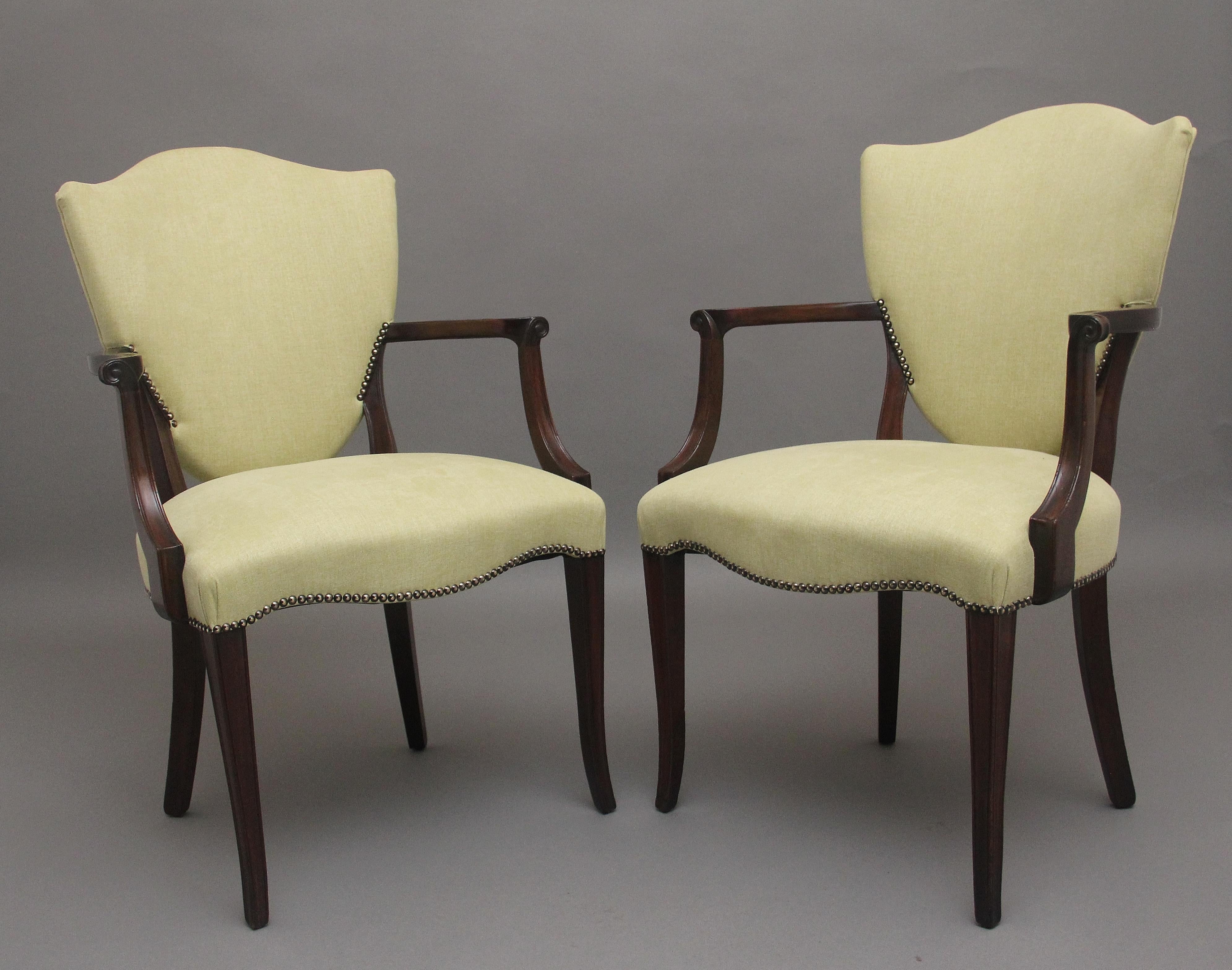 A pair of early 20th Century mahogany armchairs in the Sheraton style, recently been reupholstered in a light green fabric, having a shield shaped padded back, wonderfully shaped arm supports, stuffover upholstered seat with brass stud decoration