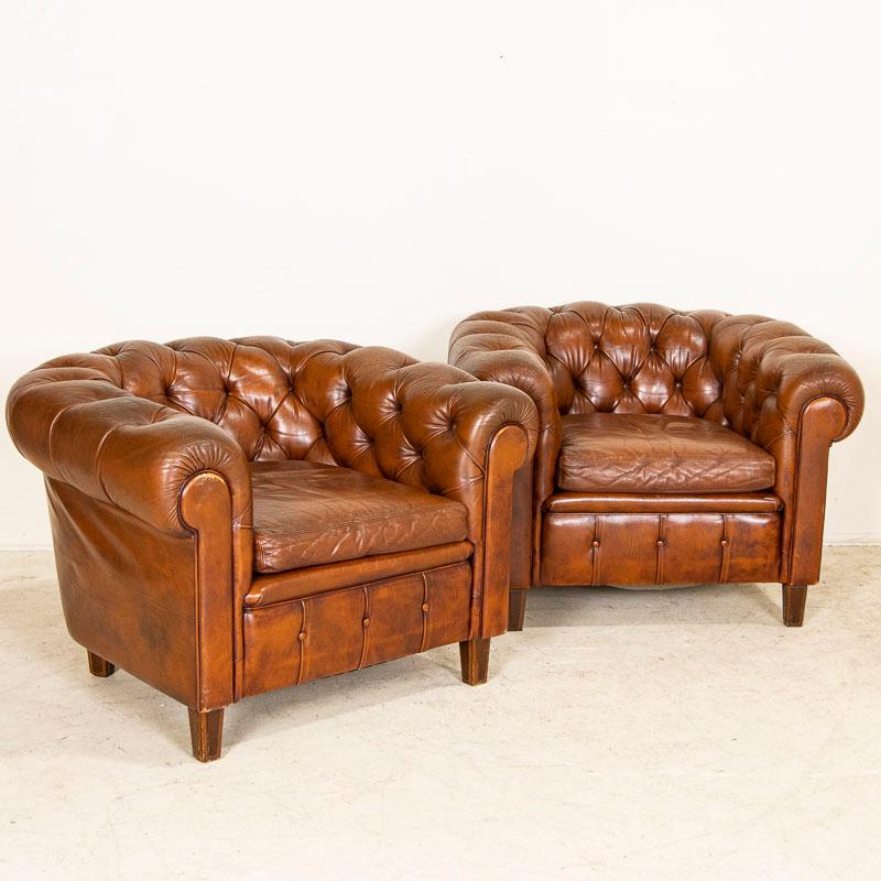 Sit back and relax in this pair of wonderful vintage leather barrel back club chairs. The rounded arms and tufted backs are accented with piping and covered buttons which are all in place. There is age related wear to the russet colored leather