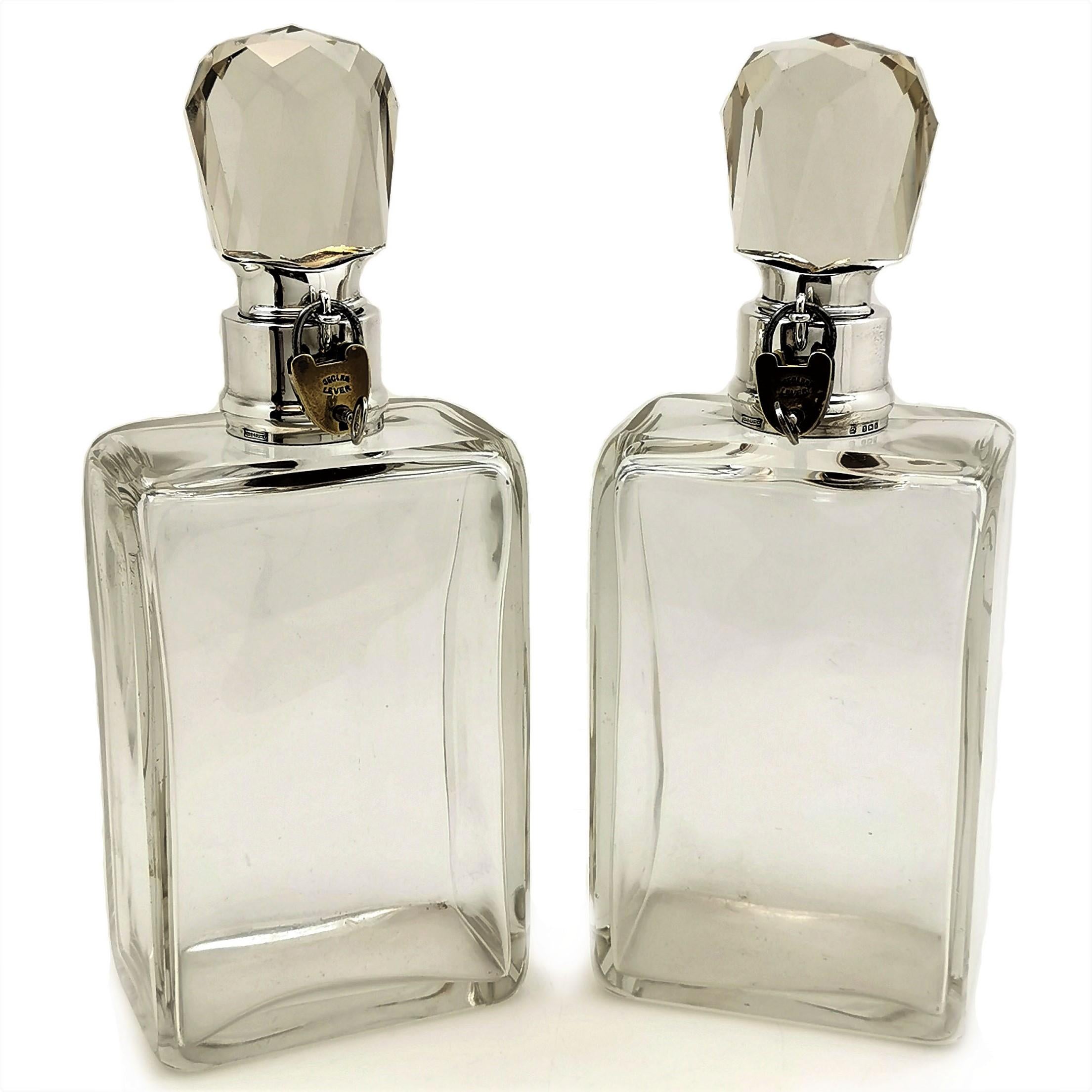 A pair of impressive Antique sterling Silver and Glass Decanters. The Decanters have rectangular clear glass bodies and faceted clear glass stoppers. The necks of the Decanters and the stoppers have fitted silver collars that interlocking clasps
