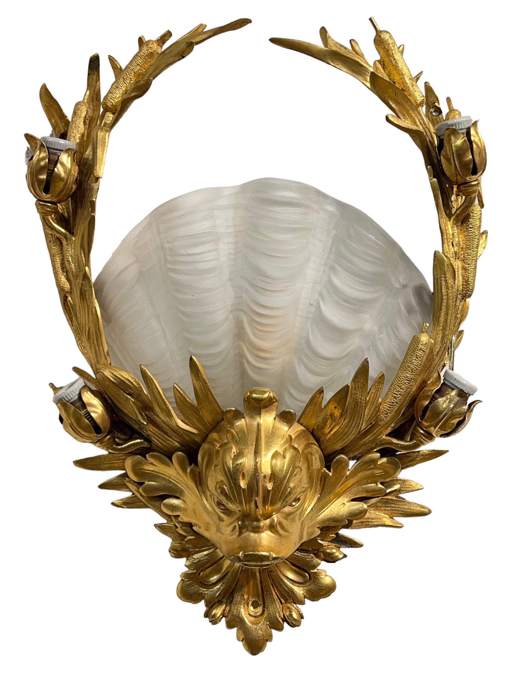 Our fabulous pair of gilt bronze sconces, circa 1905, were designed and made by Edward F. Caldwell. They feature a neoclassical design with dolphin masks and bull rush reeds, plus large scallop shell-form frosted glass shades. Each with their