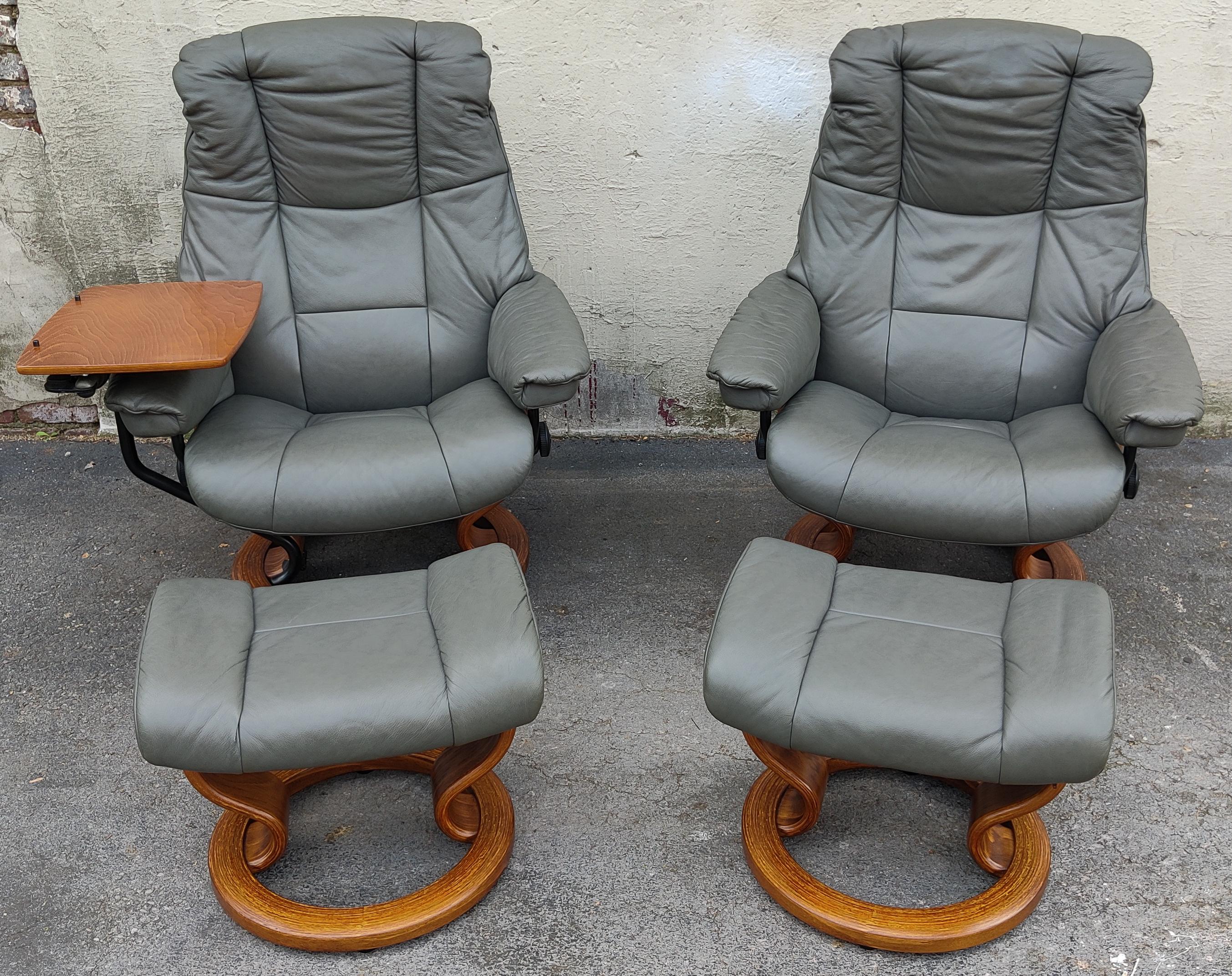 A Scandinavian style pair of recliners and ottomans by Ekornes, their Stressless brand. With teak wood and metal frames and genuine leather upholstery, these comfortable slate colored leather recliners swivel 360 degrees and feature robust lean
