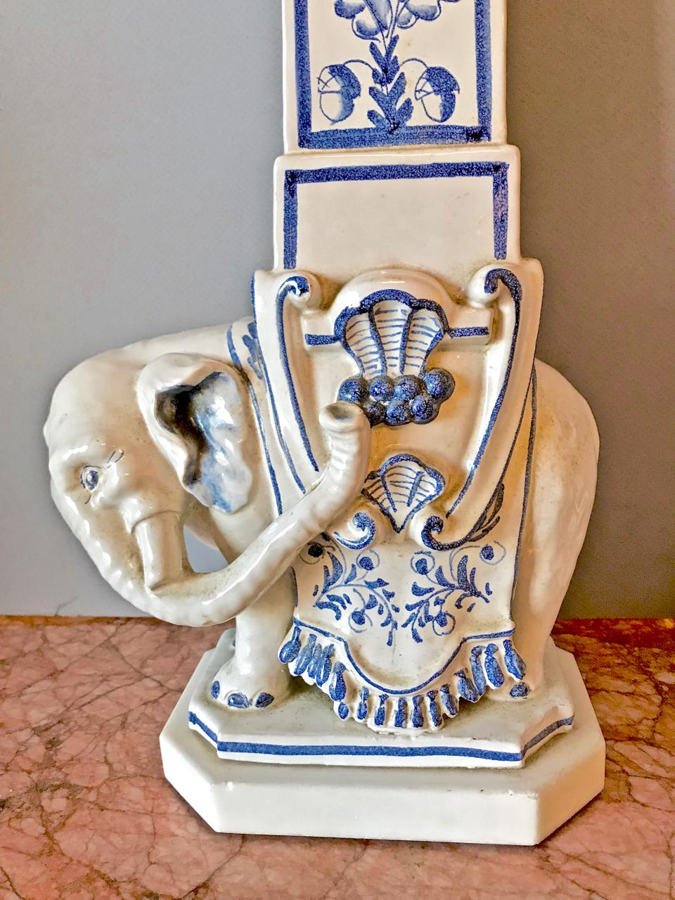 This is a stunning pair of large Italian ceramic lamps inspired by the obelisk found in the Piazza di Minerva, Rome. The midcentury blue and white pottery features a well-sculptured Indian elephant supporting a tall obelisk with neoclassical style