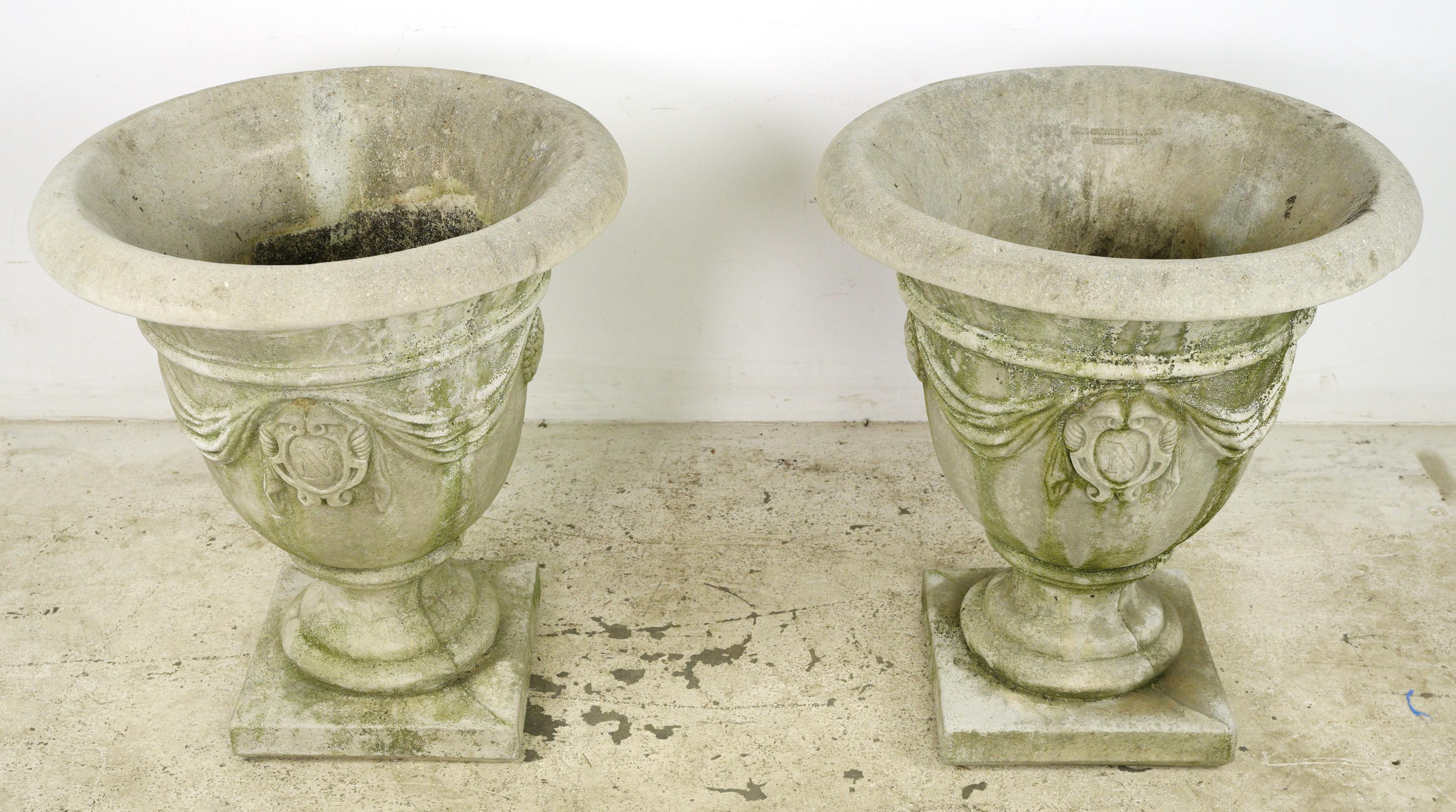 This pair of urns weere collected from an estate located in Greenwich, Connecticut. These planters feature an urn shaped design. The drapery detailing enhances the visual appeal, making them stand out as emblematic pieces. 
Whether planted with