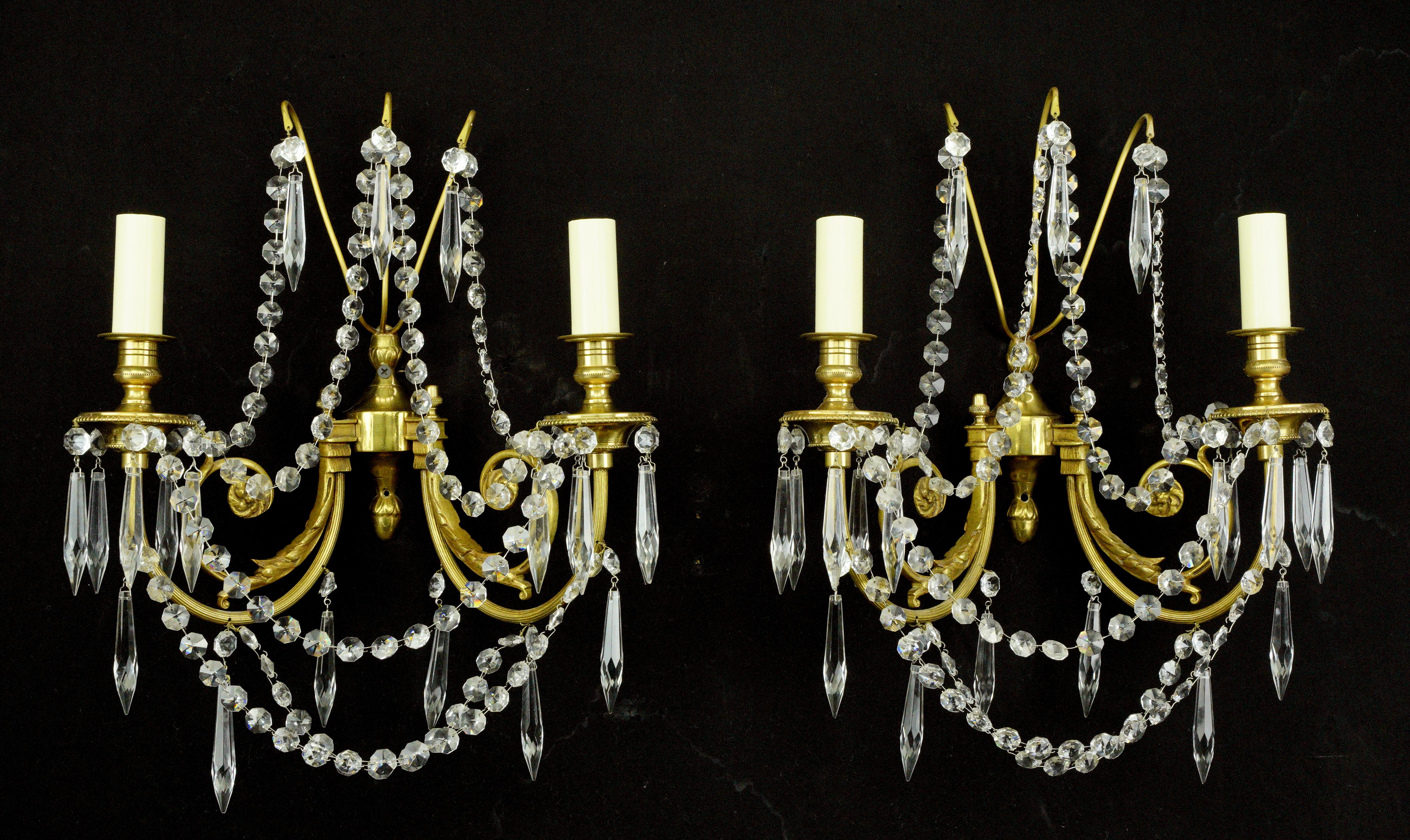 Questi pezzi sono stati acquistati da una tenuta situata a Greenwich, nel Connecticut. Coppia di applique a due bracci in stile Impero con struttura in ottone spazzolato e cristalli sfaccettati a forma di ghiacciolo e drappeggiati. Ogni applique