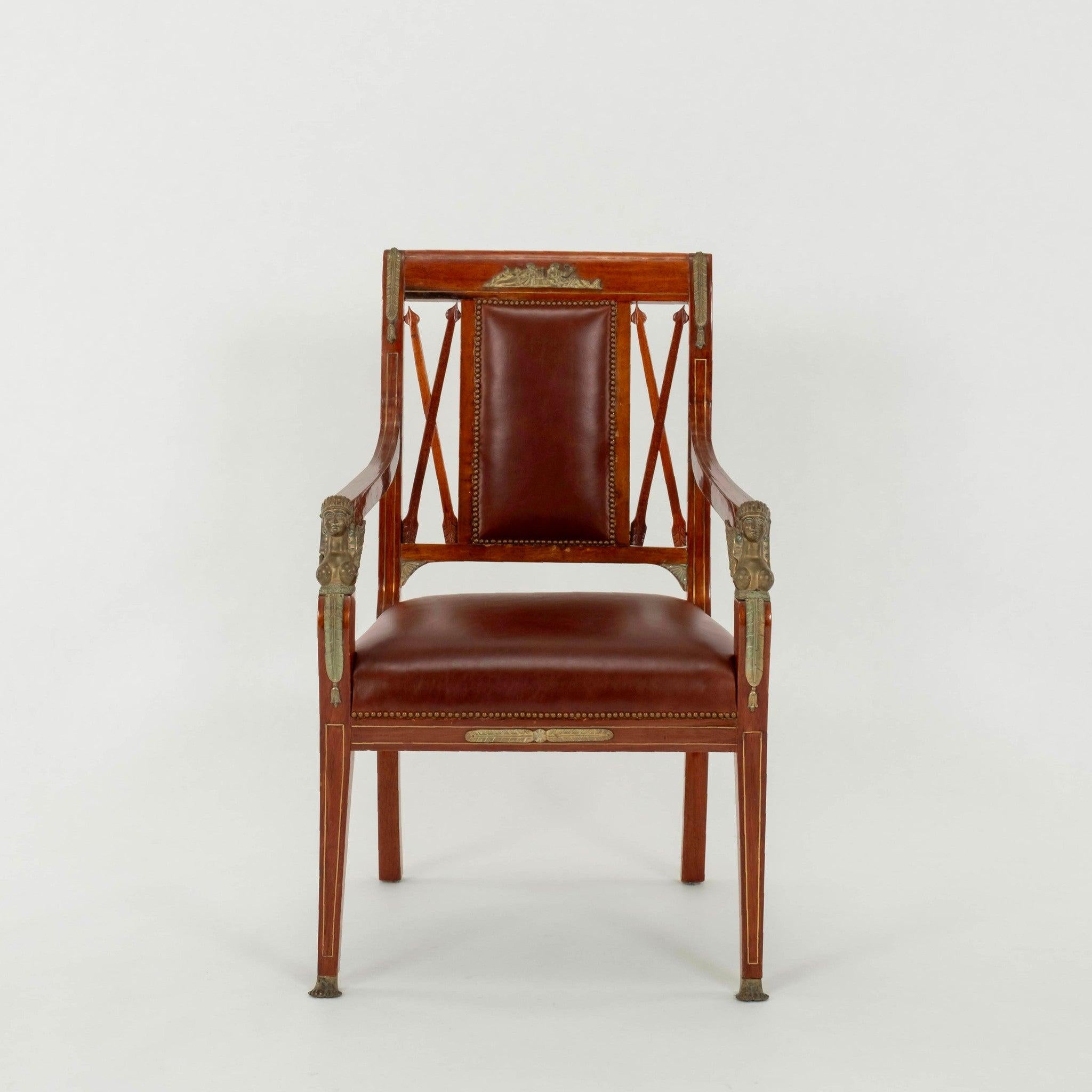 A handsome pair of  Empire Revival style mahogany armchairs featuring arrows, bronze ormolu and newly upholstered in a dark amber whiskey colored leather with nailhead detail