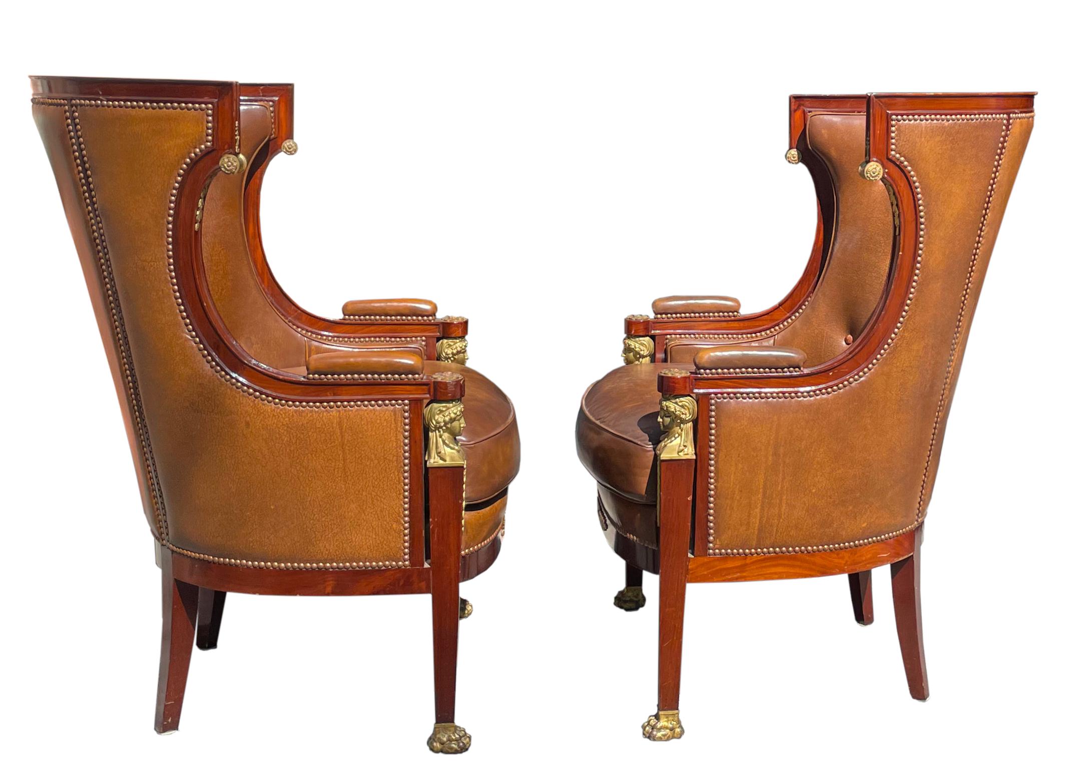 
Pair Empire Style Leather-Upholstered Gilt Bronze Mid. Mahogany Bergere
French, Circa 1900. Each curved back with tufted brown leather upholstery, continuing around to the sides, the molded rails and arm supports with gilt bronze foliate and