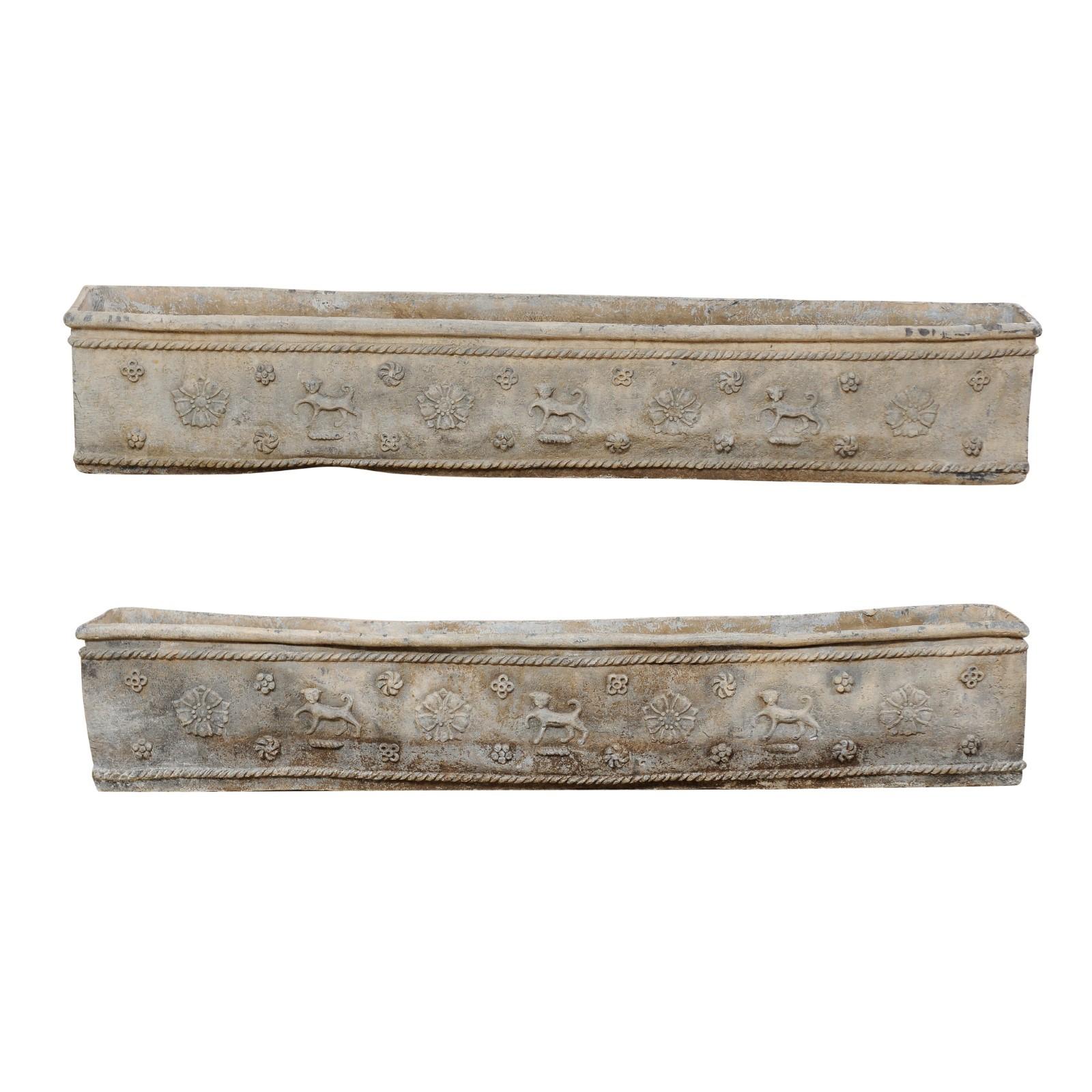 A pair of English early 19th century decorative elongated window boxes. These antique lead planter boxes from England are adorned on the front and two sides with prancing dogs and flowers, all surrounded within a roped trim outline. The back side of