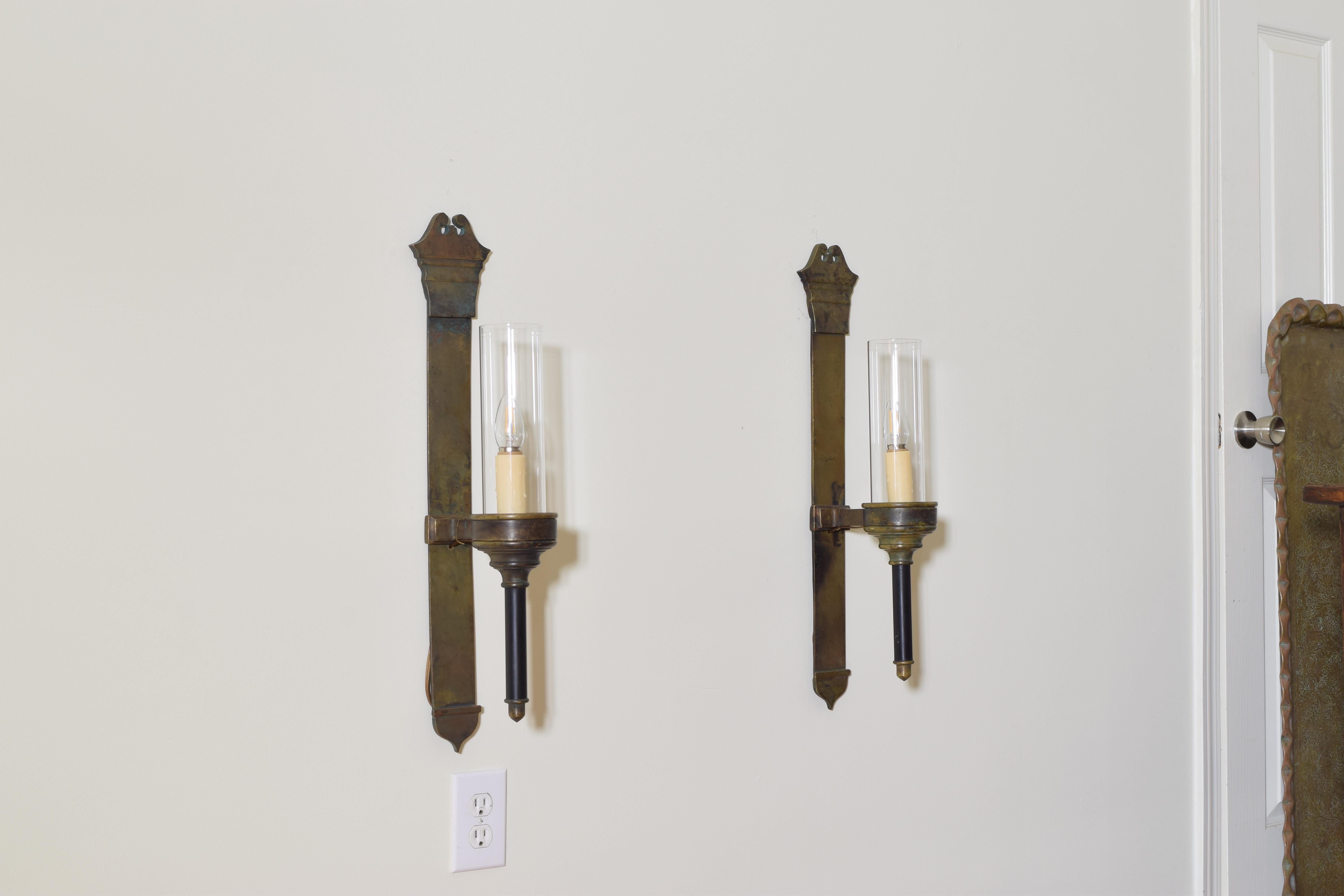 Having tall vertical back plates with shaped tops, the round bobèche extended off the backplate and having painted torchere bases, out wired, UL Wired, the glass shades of a later date, 19th century.