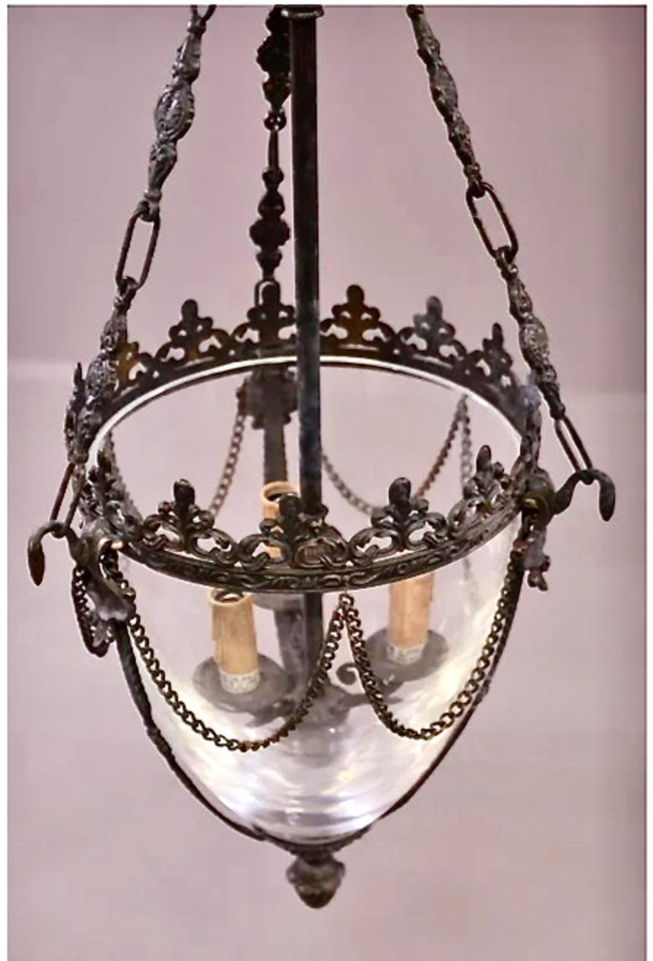 This is a pair of Regency-style bronze bell jar hall lanterns. The lanterns features a crystal bell jar supported by bronze fittings with an applied patina; the side decorative chains are removable. The fixtures were created in Italy in the late