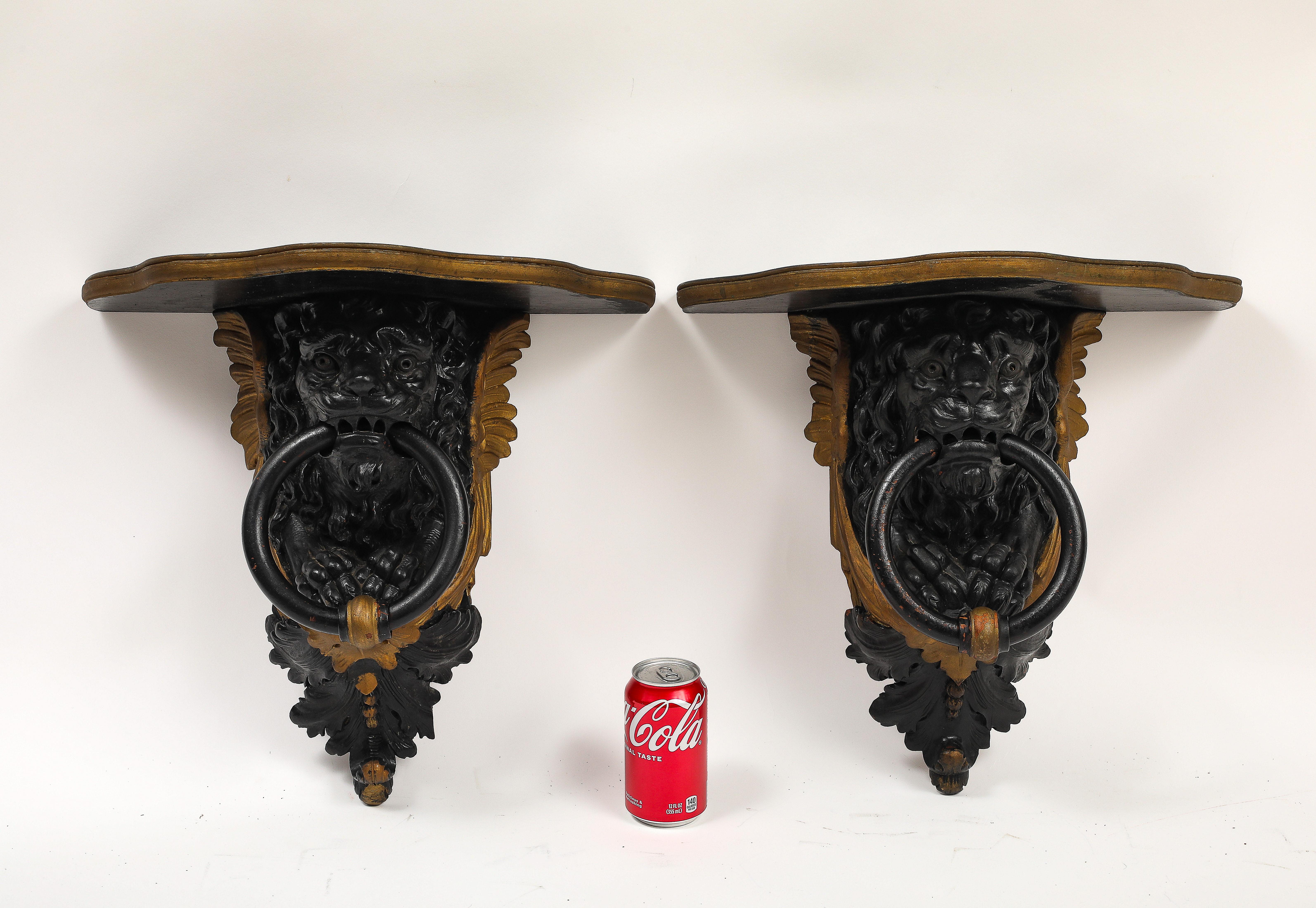 Coppia di mensole da parete inglesi Regency in lacca nera e dorate con maschere di leone intagliate a mano e anelli Looping. 

Ogni staffa è strutturata con un ripiano piatto e sagomato sostenuto da un supporto sporgente intagliato. I supporti sono