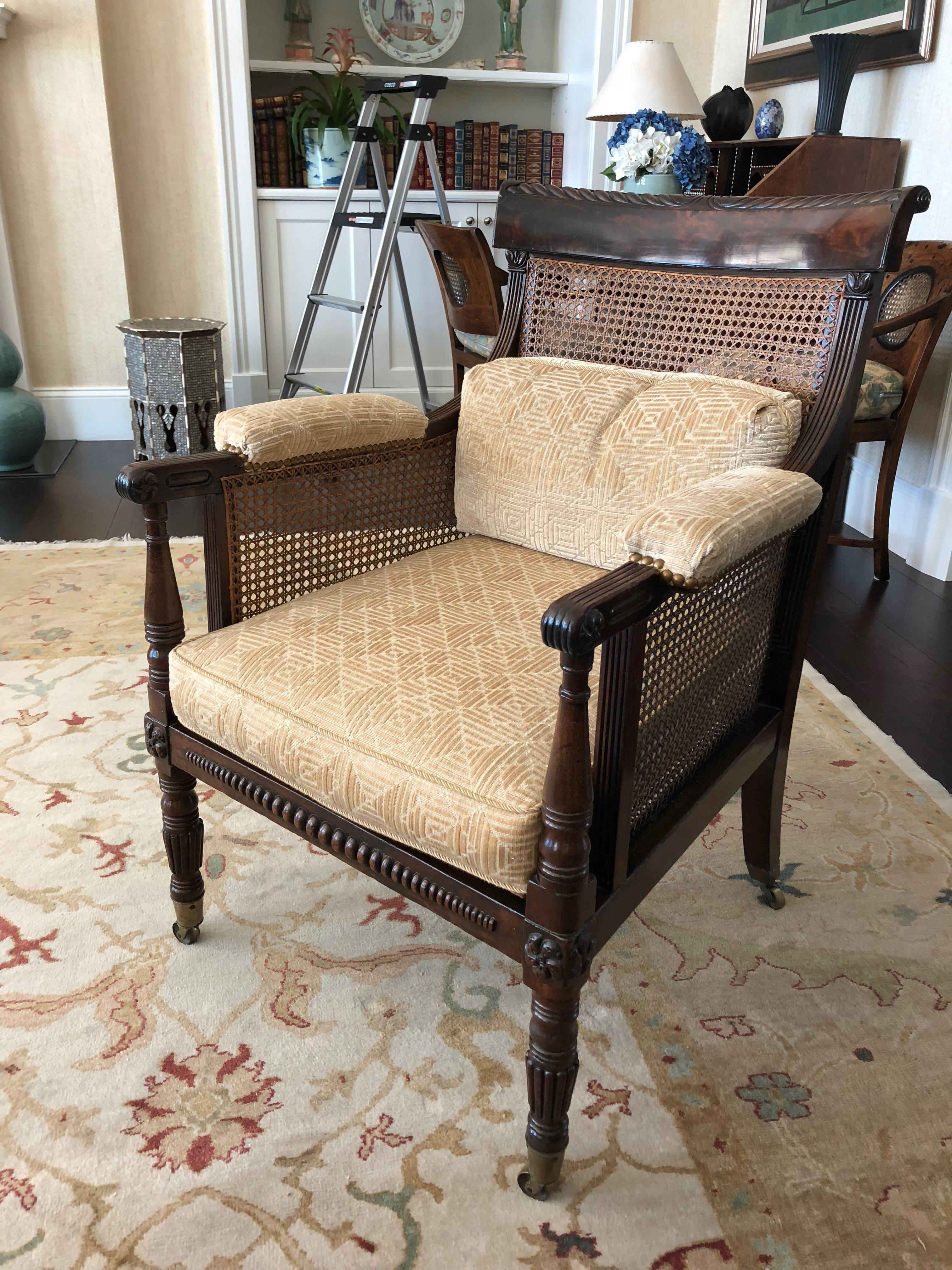 This is a pair of Regency caned library armchairs bergere (off pair--not exactly alike) mahogany with broad back rails caned inset to back, sides and seat having padded arm rests, front legs carved and turned all legs on brass casters purchased in