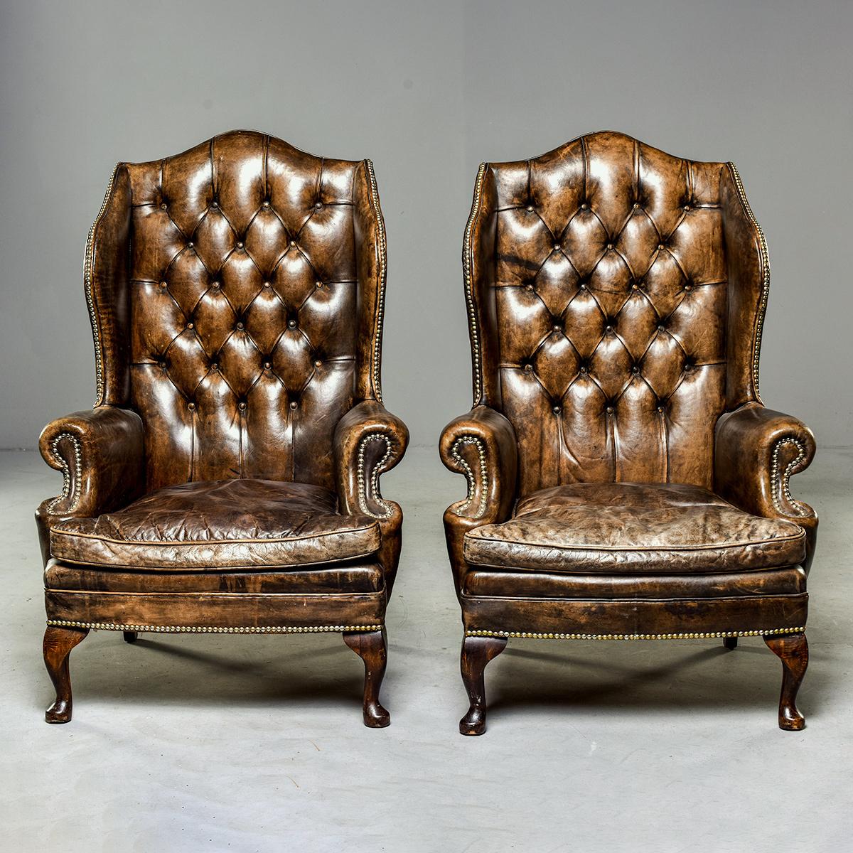English pair of leather armchairs with tall, tufted and winged seat backs, rolled arms, cabriole legs, brass nailhead tacks and removable seat cushions, circa 1920s. Original leather in very good condition with nice patina, frames and structure are