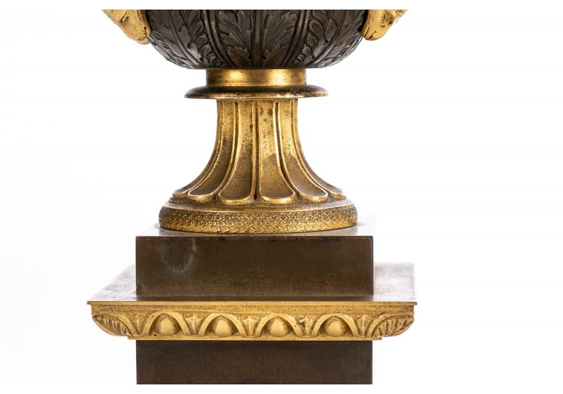 Fine pair of Campana urns with gilt egg-and-dart rims, handles with ram's head attachments, and leafy bases on fluted gilt stemmed feet. The tall pedestals with gilt egg-and-dart ledges and applied wreaths with ribbons. 
Measures: Height. 14 1/2