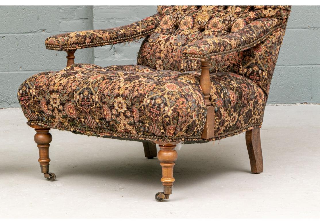 Quality comfortable wide and low armchairs, the arms with turned supports and raised on turned front legs on casters and curved square back legs. Upholstered in a machine made tapestry fabric in a dense brown and gold floral print, tufted on the
