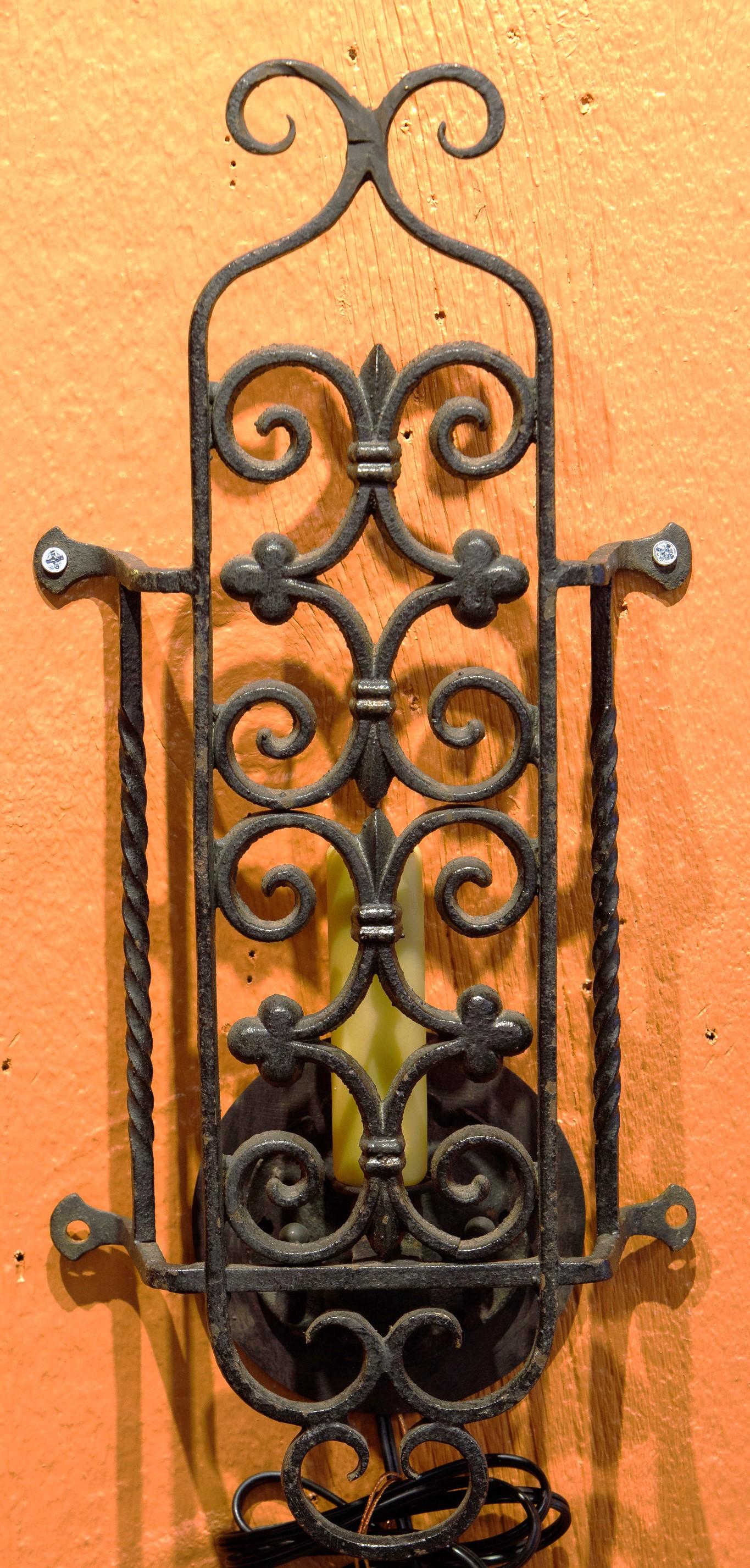 
This pair of iron sconces has a classic Spanish Colonial Design.  The candle appears behind the grill that has simple scrolls and trefoils.  There is a bit of gilding on the grill.  There are arms that may be screwed into the wall.  Sconces have