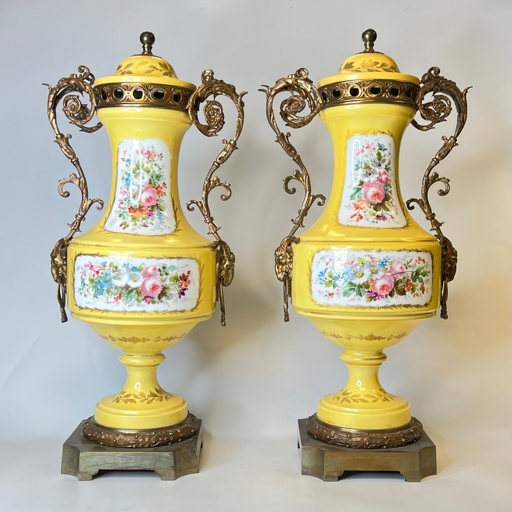 Paar französische, in Bronze gefasste Porzellanurnen im Stil von Sèvres aus dem 19. Jahrhundert im Louis XV/XVI-Stil mit fein gemalten Kartuschen, die Liebespaare und Blumensträuße darstellen.
