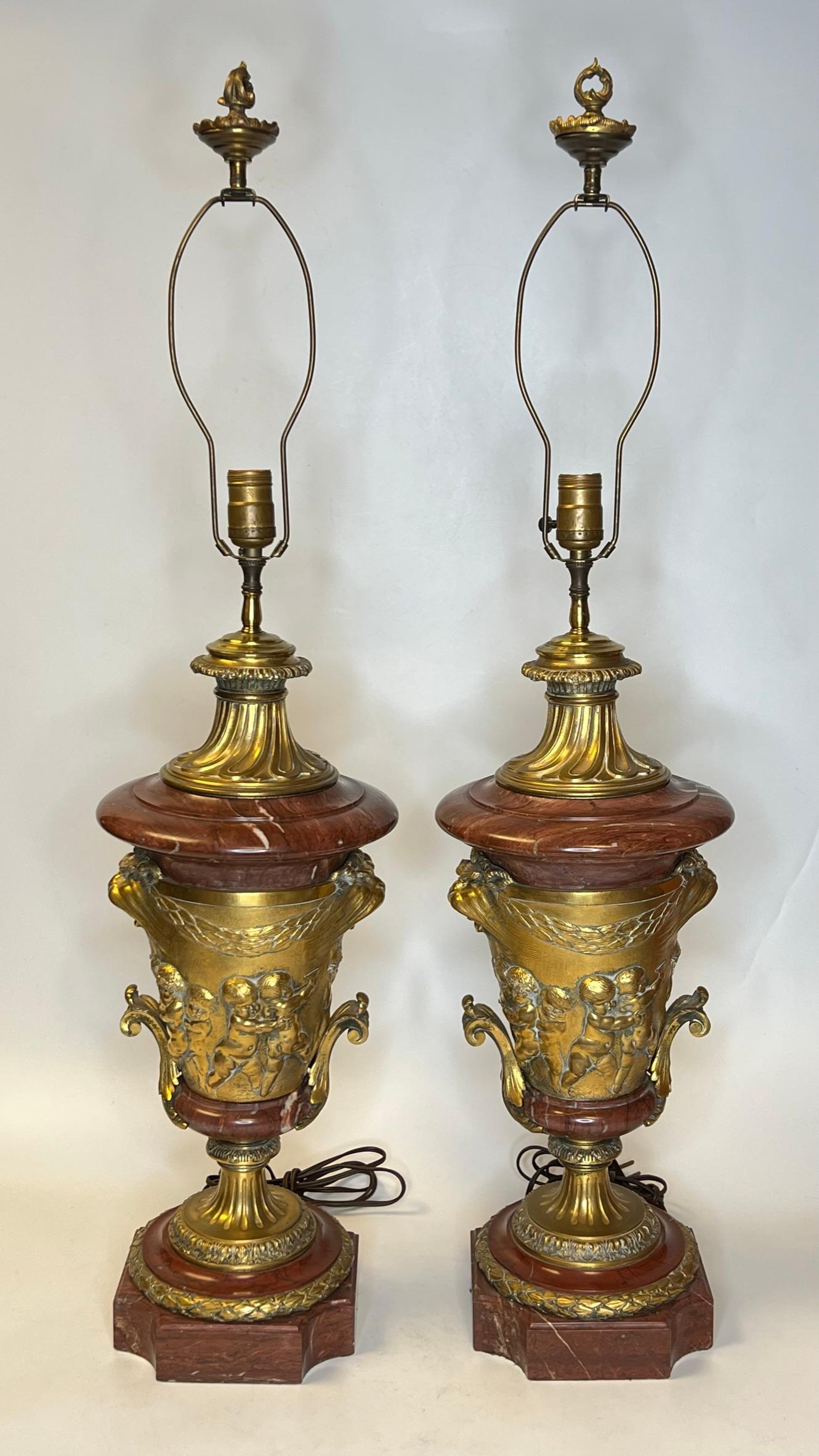 Pair of very finely cast and large French 19th century gilt bronze and rouge marble table lamps with frolicking putti and prominent lion masks.