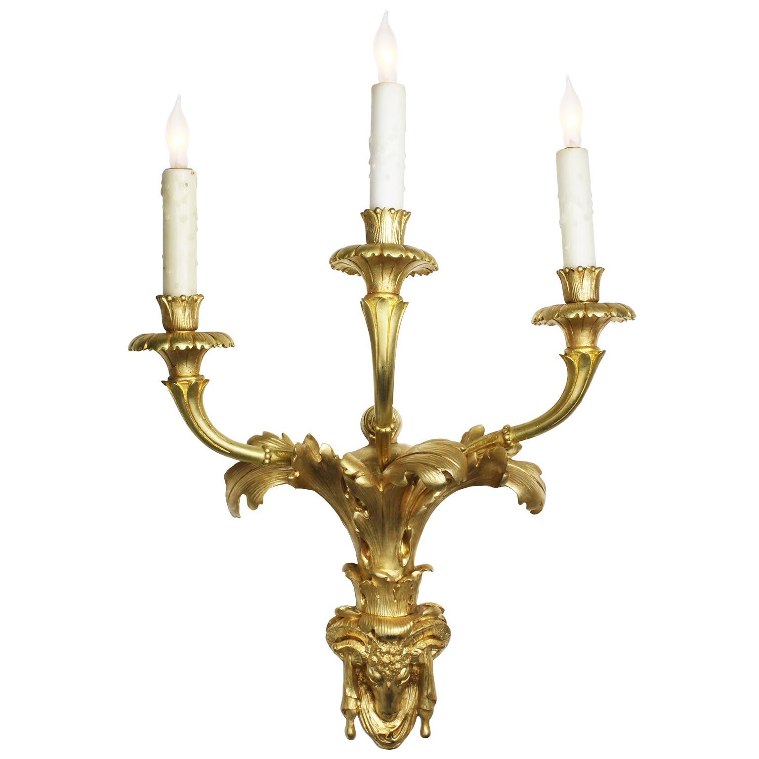 Une belle paire d'appliques murales à trois lumières en bronze doré de style Régence du 19ème siècle. Les chandeliers à trois lumières, maintenant électrifiés, surmontent un motif de feuilles d'acanthe se terminant par un fleuron drapé en forme de