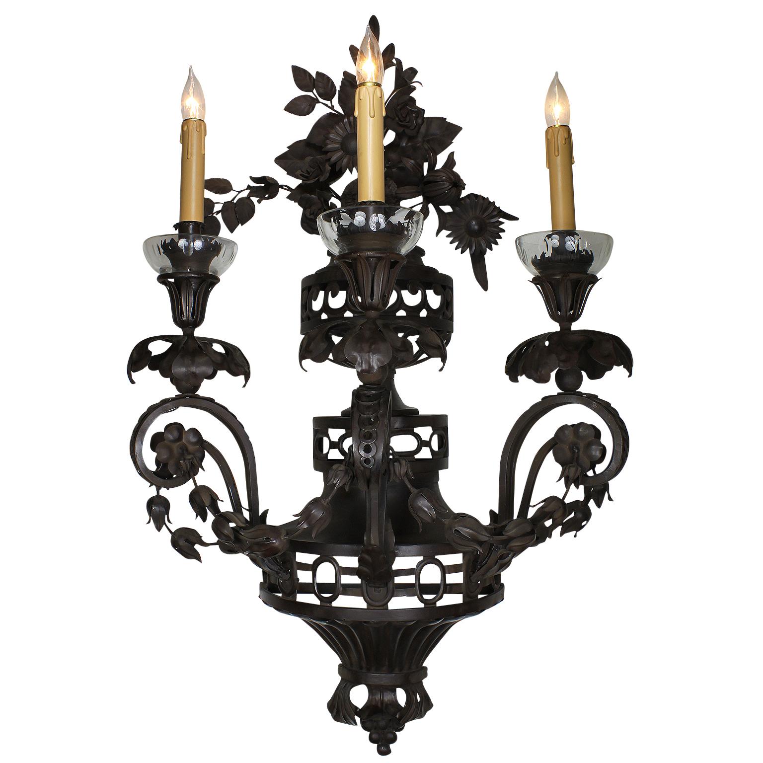 A large and rare pair of French 20th century Rococo Revival style patinated metal three light wall sconces. The urn shaped wall lights in a dark brown patina with three scrolled candle-arms conjoined with flower wreaths and cut-glass wax-holders,