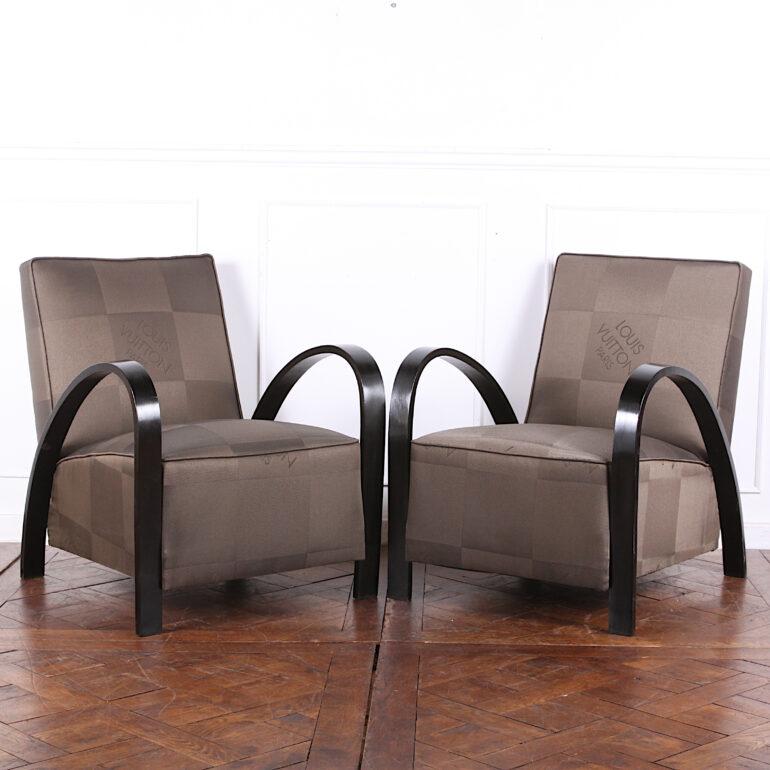 A pair of French Art Deco armchairs, the boldly-curved arms with ebonized finish and recently upholstered in 'Louis Vuitton' themed fabric.
