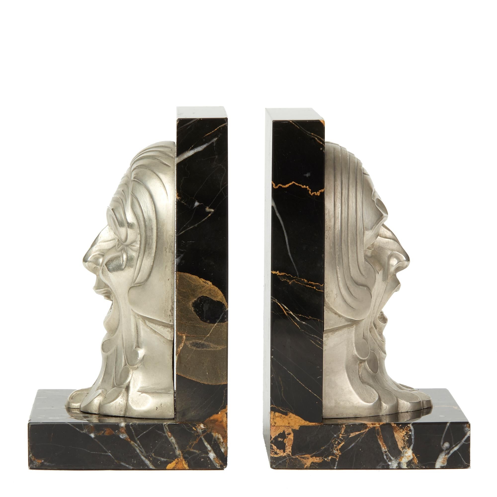 A very stylish pair of French Art Deco marble mounted bookends with moulded polished alloy masks, one depicting comedy and the other tragedy. The masks are mounted on an L shaped black marble stand with orange and white veining and are not marked.