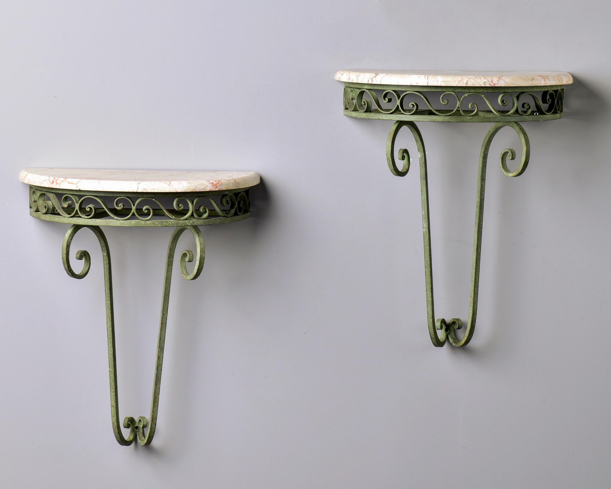 Circa 1930s pair of French wall-hung demilune consoles with iron frames in original green finish and marble tops in shades of cream and white with dark gray and apricot streaks. Unknown maker. Sold and priced as a pair. Unknown maker. Sold and