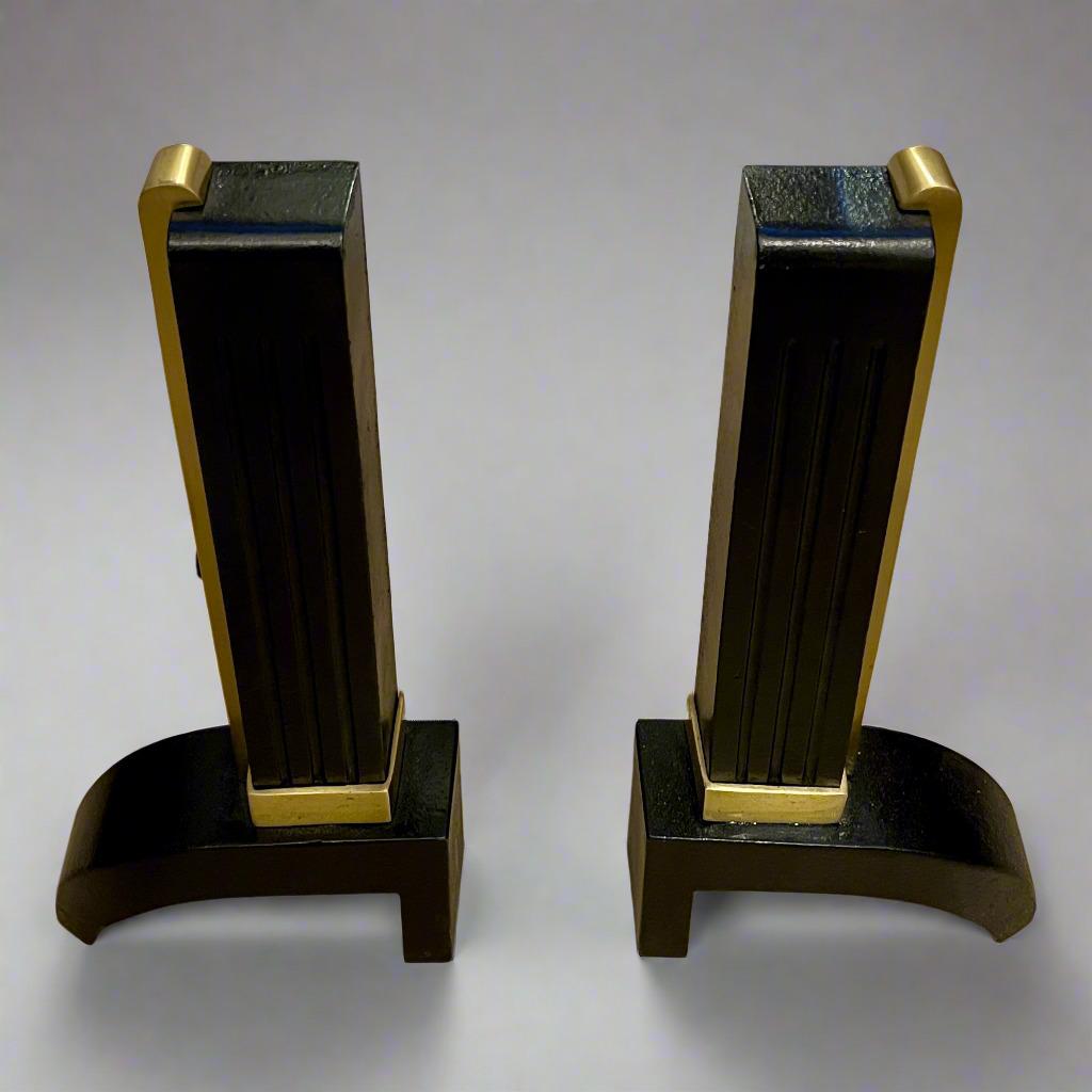 A pair of handsome modern Art Deco period andirons from France circa 1930. Each piece is made of heavy cast iron and defined by the powerful line of patinated brass seen on each andiron. The strong vertical shaft stands atop a curved lower support