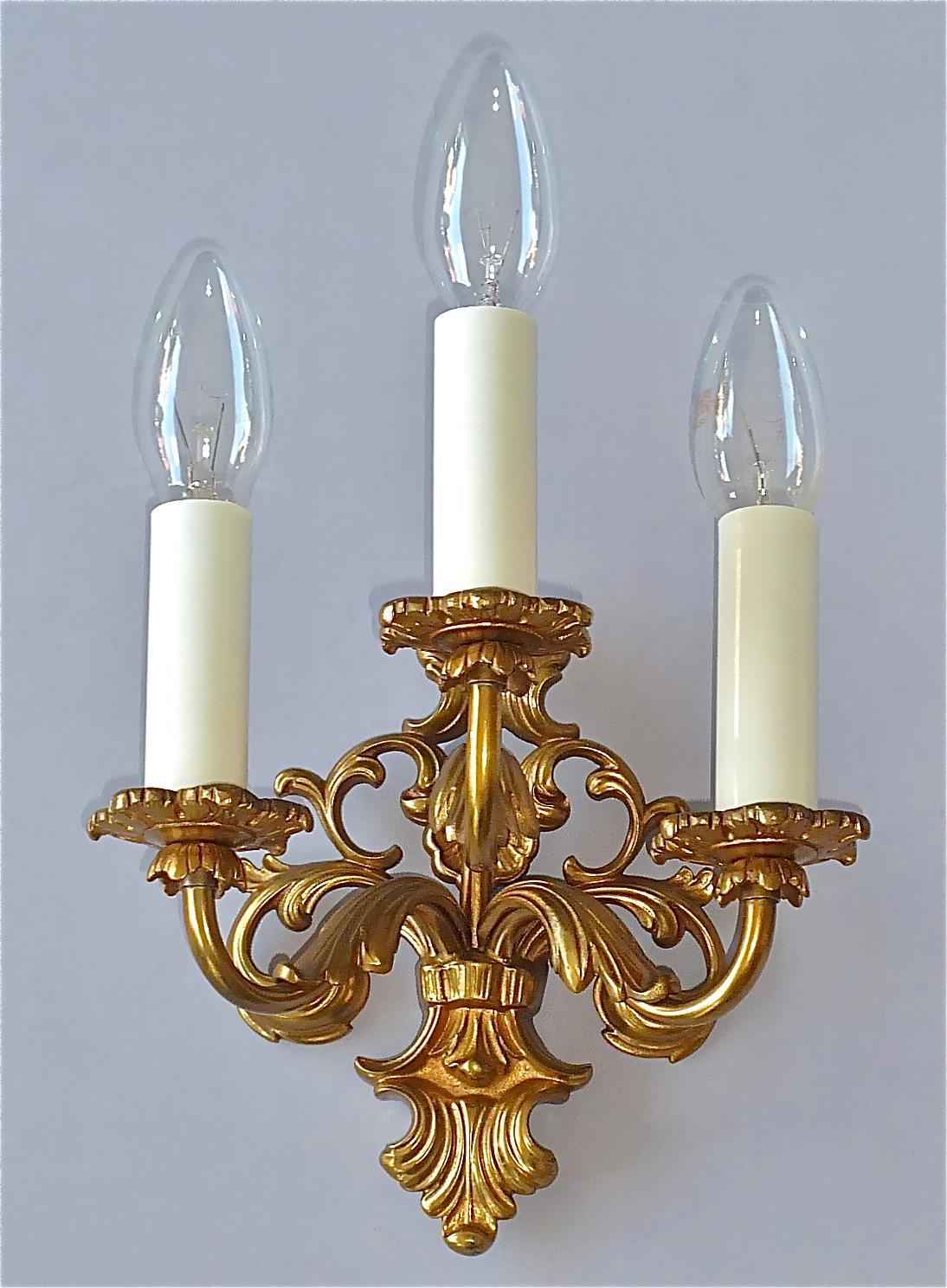 Elegant and fine pair of floral three-arm gilt bronze metal Baroque / Rococo style wall lights or sconces, possibly Maison Bagues, France circa 1950s. The beautiful and classical lights with the typical decor of this period are new rewired, so fine