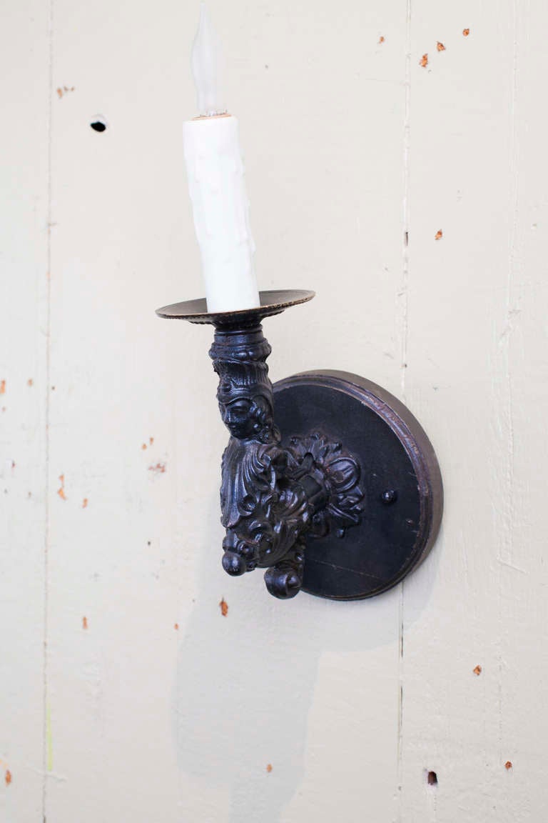 Pair of French black iron figural wall sconces (circa 1900): this pair of charming, heavy cast-iron sconces with bust of figure on the arm, Finish is original, and sconces are newly wired in the USA with a candelabra socket and all UL listed parts.