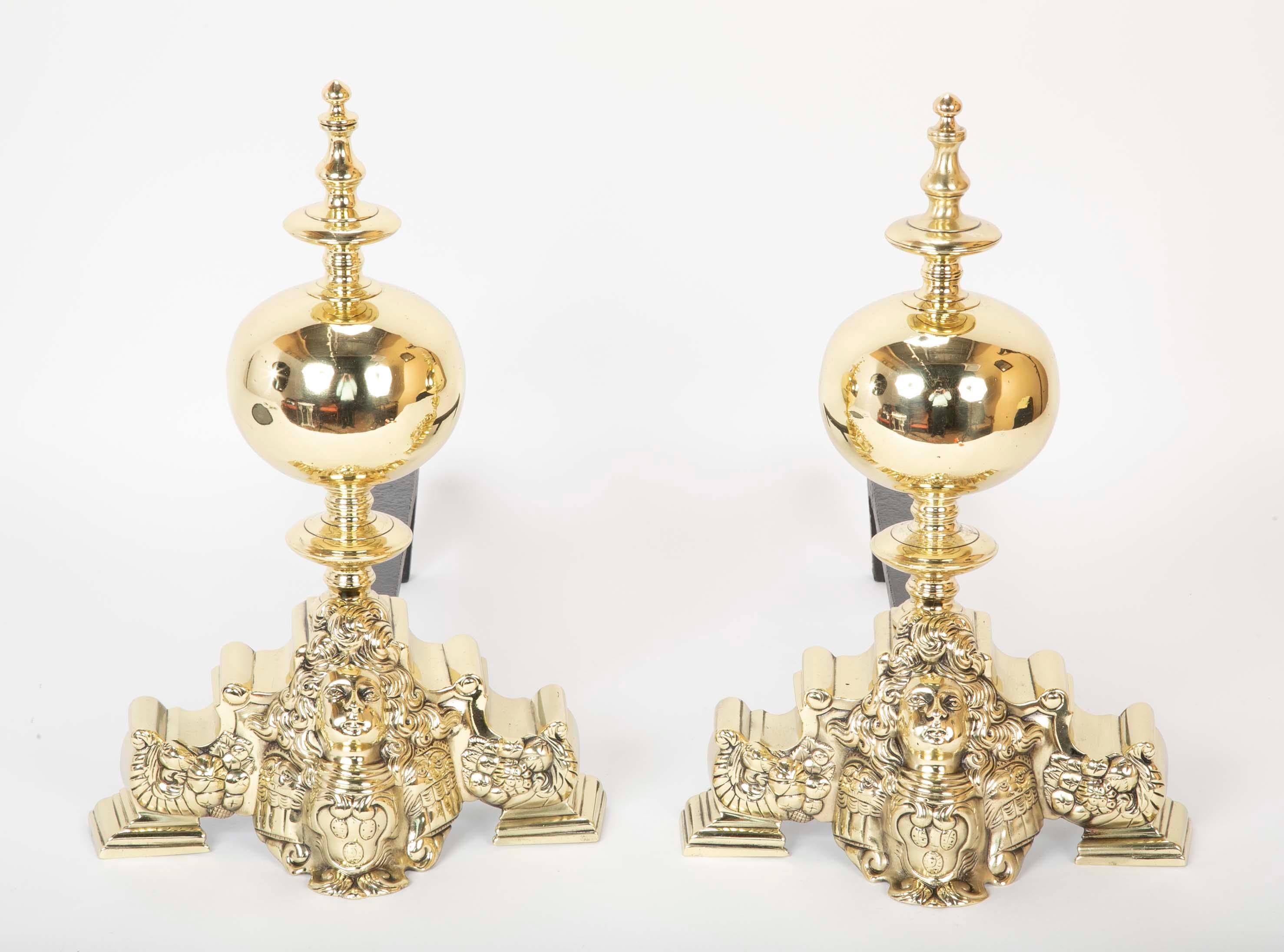 A handsome pair of small scale French Rococo style bronze chenets, the base depicting a male face with flowing hair, perhaps a portrait of Louis XV, above an armorial, flanked by lion masks and cornucopia. Topped by a large ball and bold turnings.