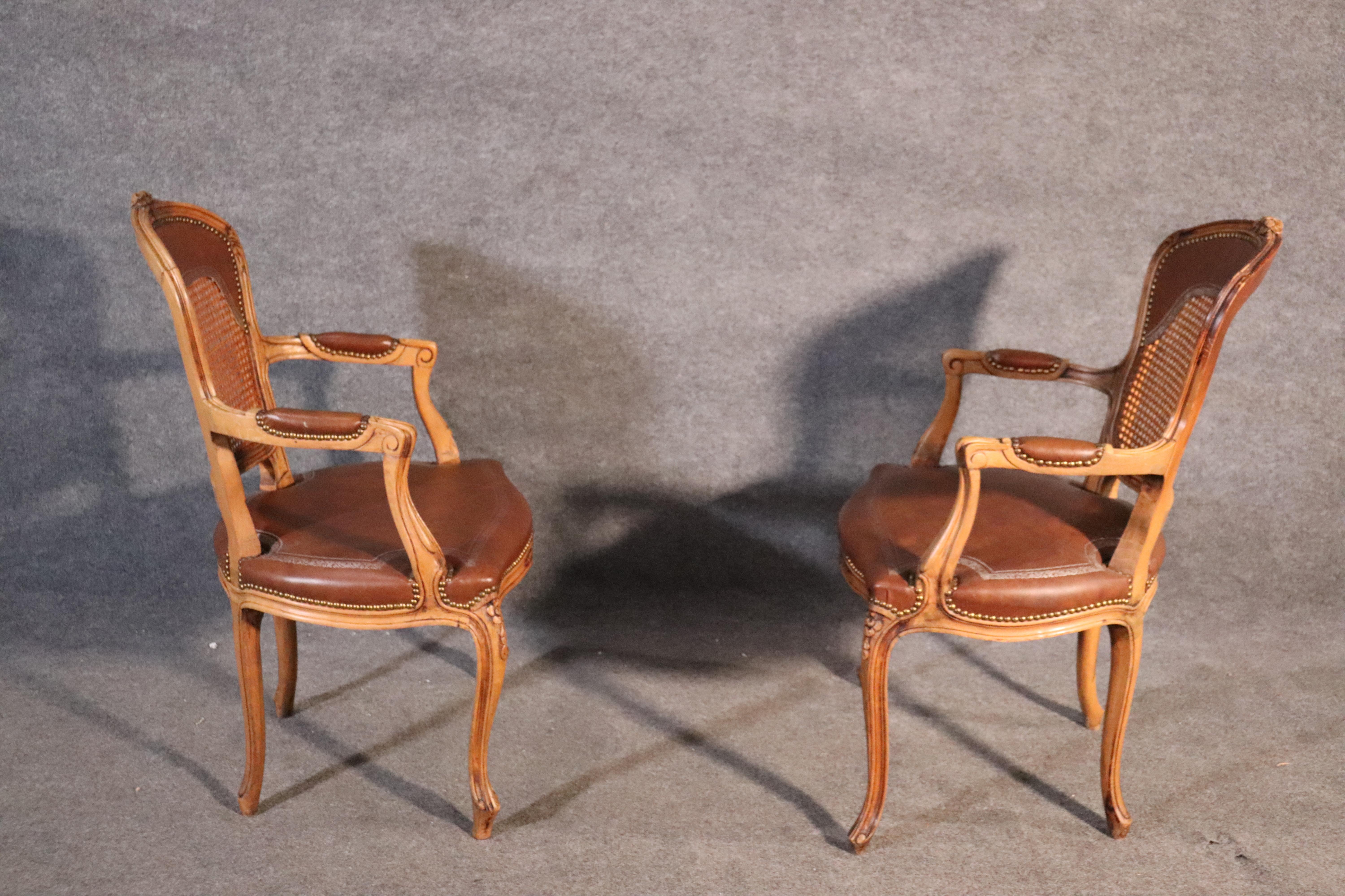 These gorgeous chairs feature beautiful caned backs and finely carved frames surmounted with carved flowers. The upholstery is simulated embossed material made to look like leather but it's not. The chairs are French and date to the 1940s era. They