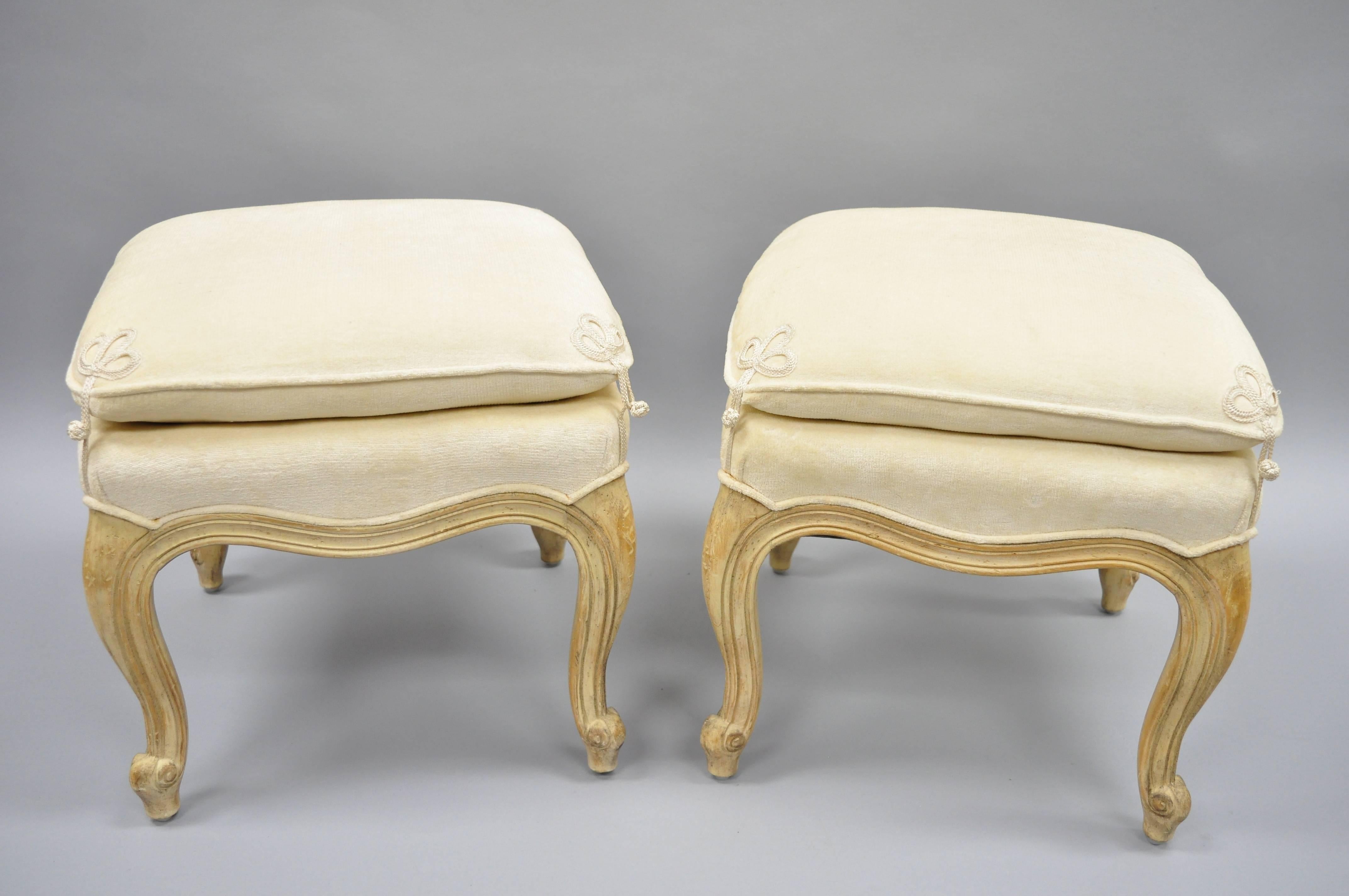 Pair of French country Louis XV style upholstered ottomans by Interior Crafts. Item features solid wood construction, cream colored attached pillow seat, distressed finish, cabriole legs, quality American craftsmanship, great style and form, circa