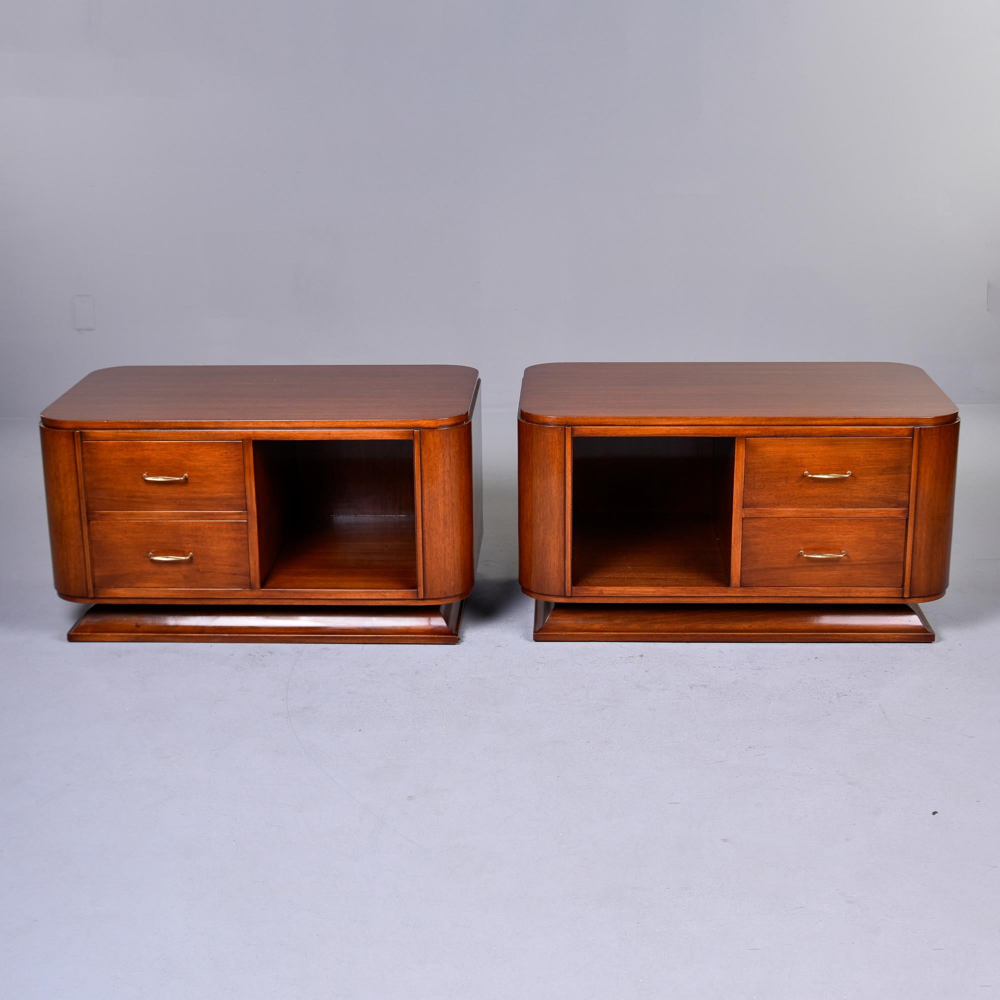 Found in France, this pair of Art Deco bedside or end cabinets date from the 1930s. These curvy cabinets are made of walnut with two drawers on one side and an adjoining open storage compartment. Wide, curvy pedestal bases and thin brass handles.