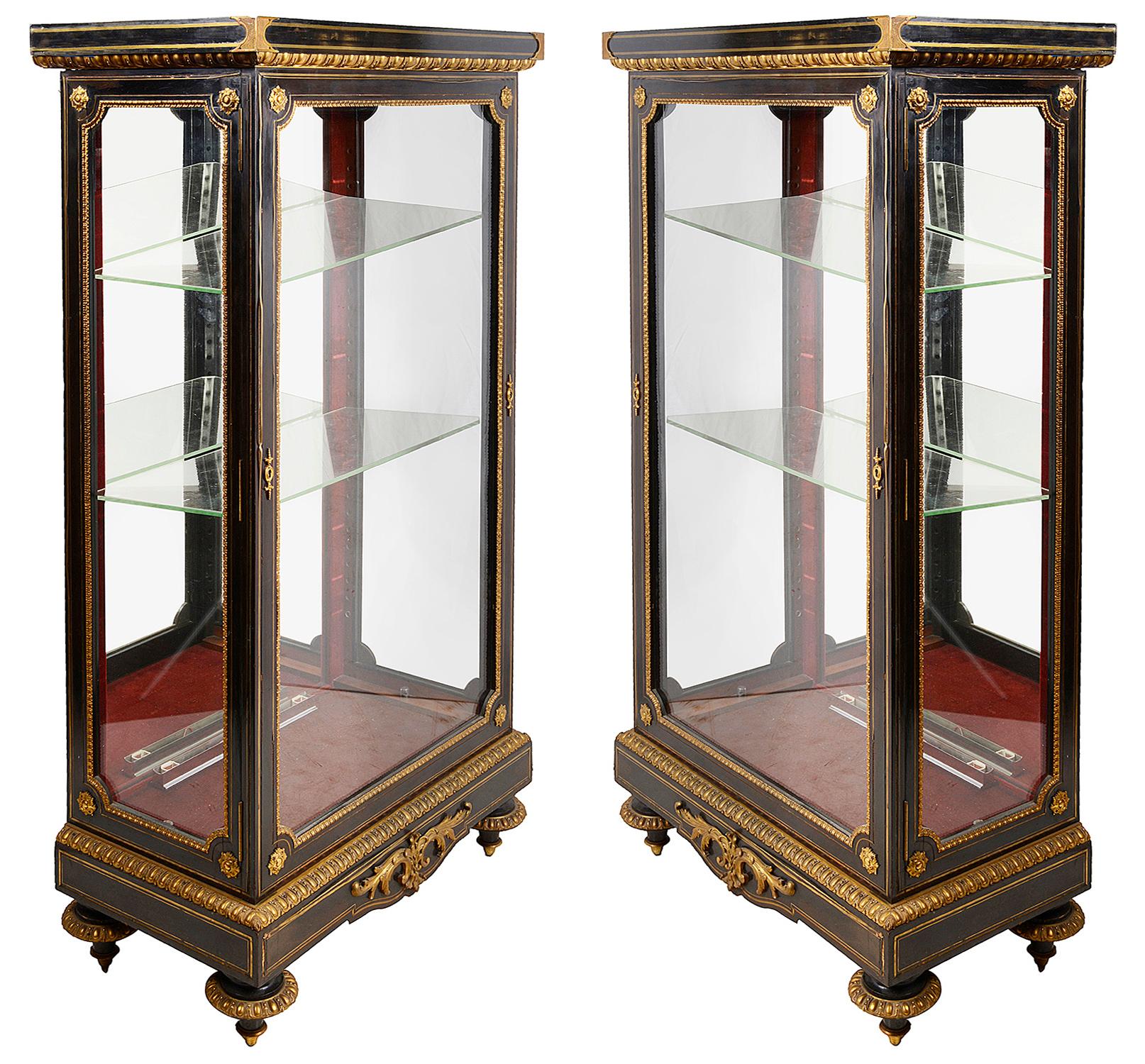 A good quality pair of 19th century French ebonized display cabinets, having classical gilded ormolu mounts. Adjustable glass shelves and mirror backs within, raised on plinth bases and turned ormolu mounted feet.
