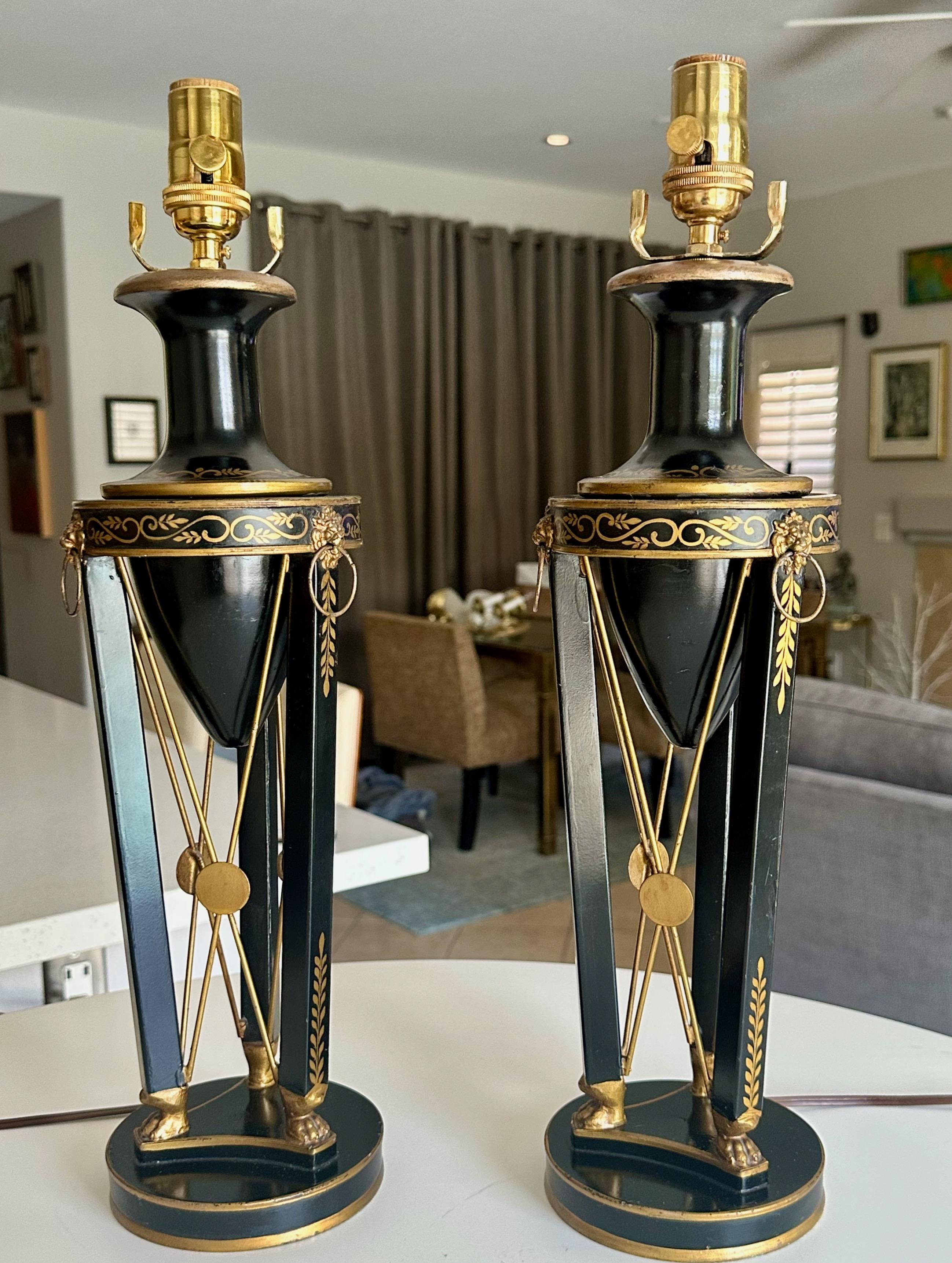 Paire de lampes de table en métal tolé noir et or de style Empire français. Les lampes de style urnes sont peintes à la main avec des détails dorés, décorées de têtes de lion et de pieds en forme de pattes. Nouvelles prises à 3 voies en laiton, les