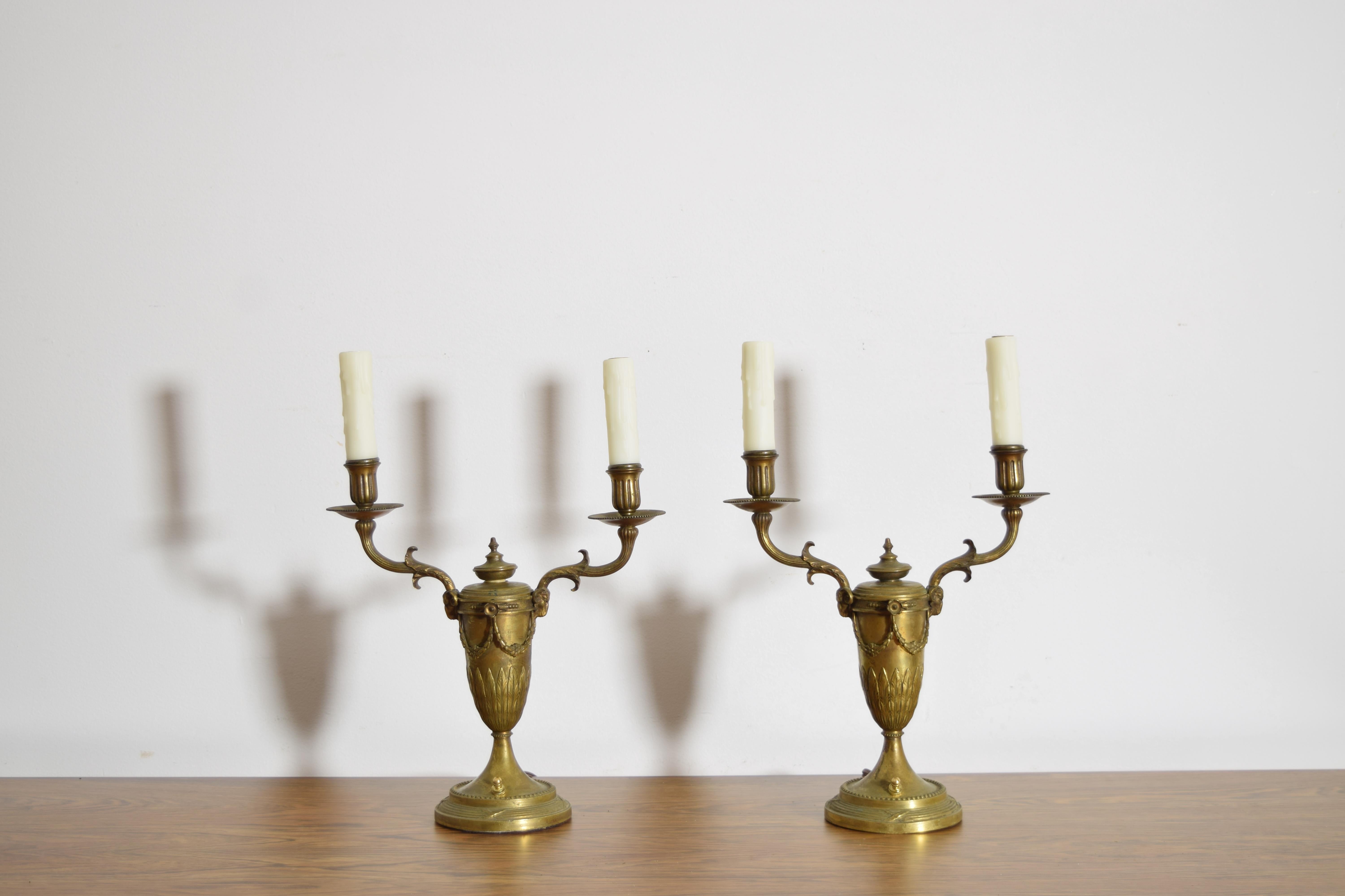 formerly oil lamps and retaining their pump primers atop the bases, having precisely cast urn-form bases issuing two arms with sockets and wax candlecovers