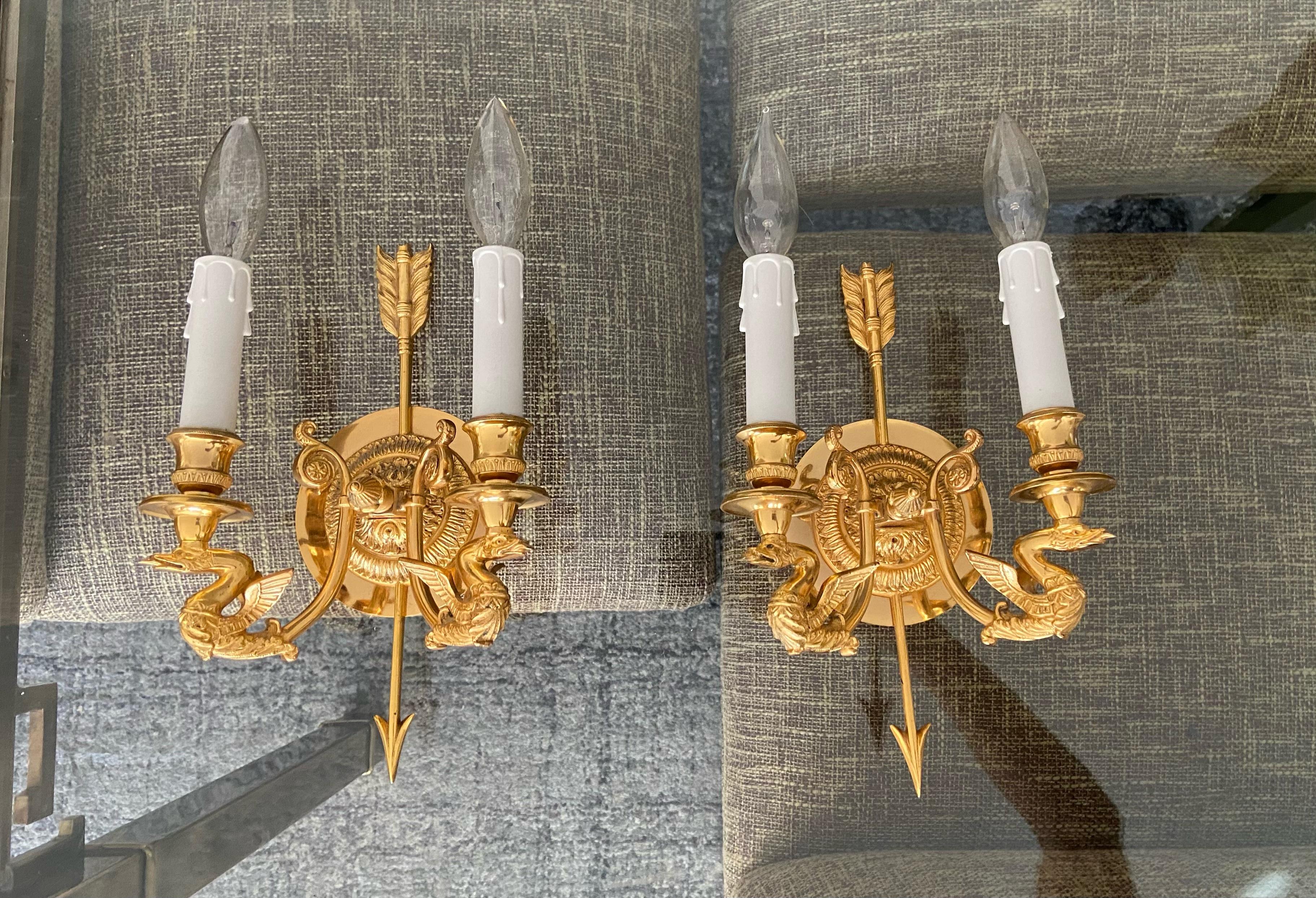 Pair of French Empire style gold plated bronze wall sconces. Expertly executed with fine detailing including arrow and swan motif. Each sconce uses 2 candelabra base bulbs. Stamped Portugal. Shades not included. Attributed to Sherle Wagner.