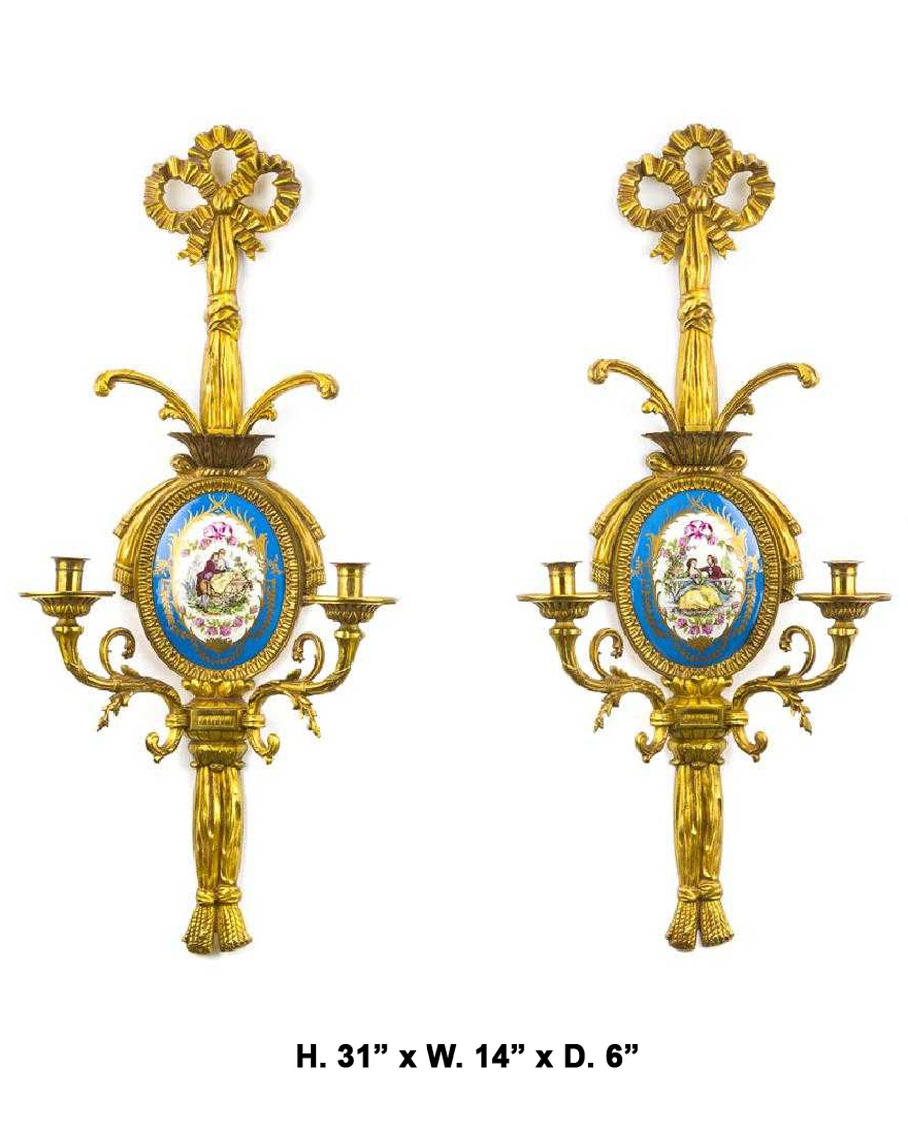 Imposing pair of French Louis XVI style gilt bronze and oval Sevres plaques two-light sconces, 20th century.
The sconces are surmounted by gilt bronze ribbons over a signed oval celeste bleu Sevres plaque depicting romantic scenes, above two