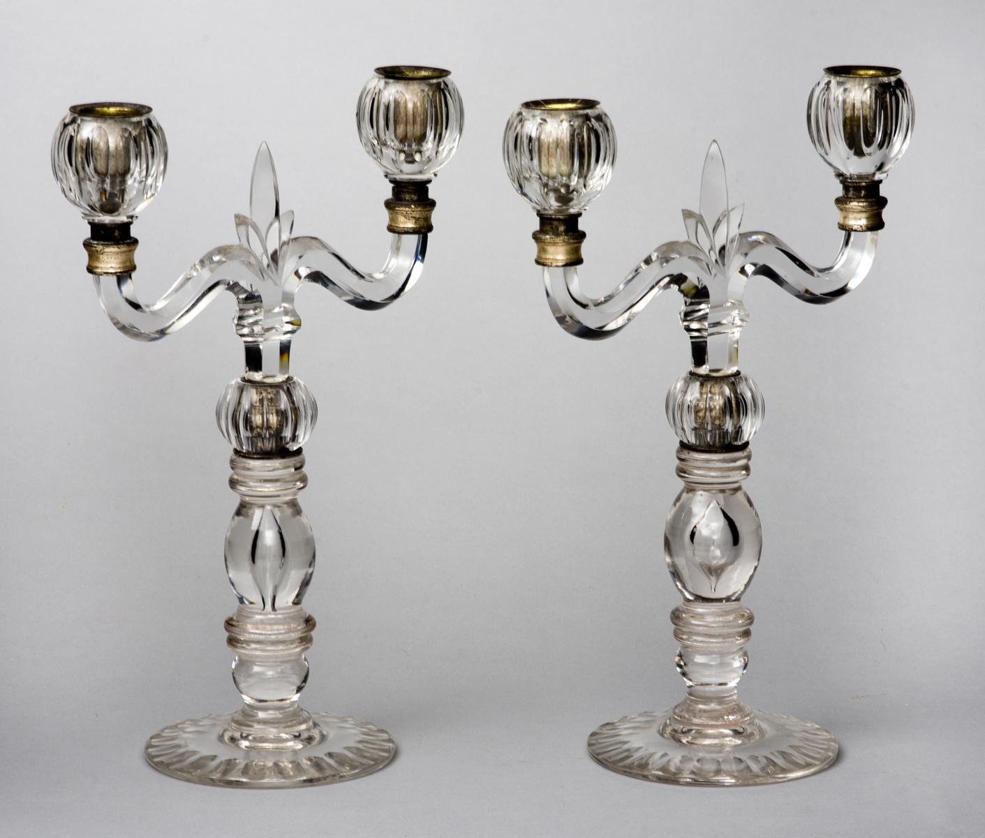 Pair of Baccarat-style molded glass two-arm candelabra with a fleur-de-lis between the arms, fluted nozzles, turned upright column on fluted base.