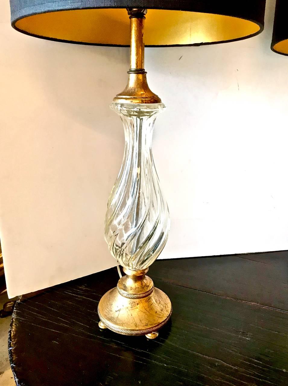 This is a super chic pair of circa 1960s swirled glass lamps that are most probably French in origin. The sparkling swirled glass is fitted with a gold leafed footed base and top. The lamps are completed with black shade with gilt interior.