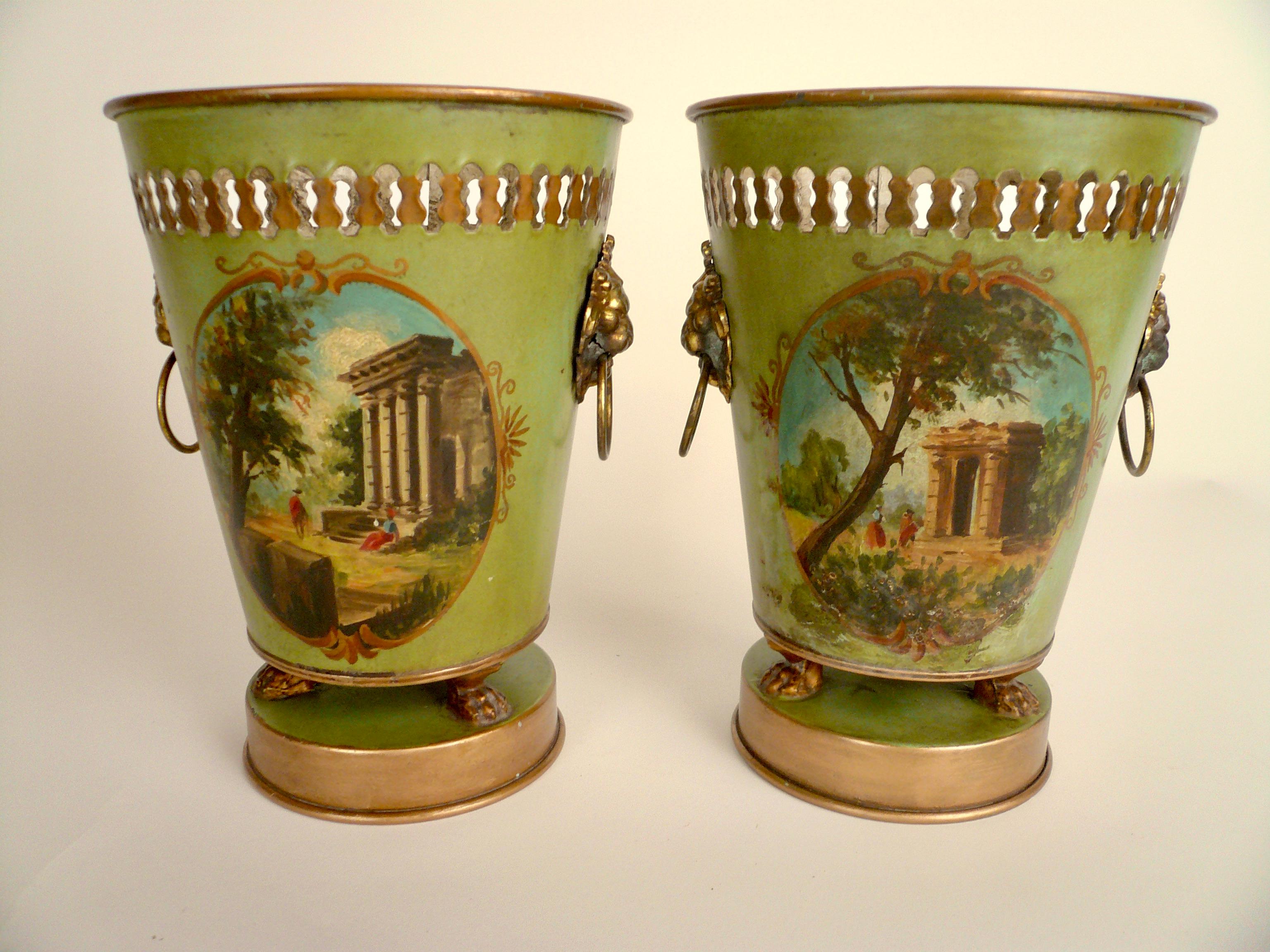 Cette belle paire de cache-pots en tole française présente des paysages classiques peints à la main, ainsi qu'une tête de longe et des poignées en laiton doré. 