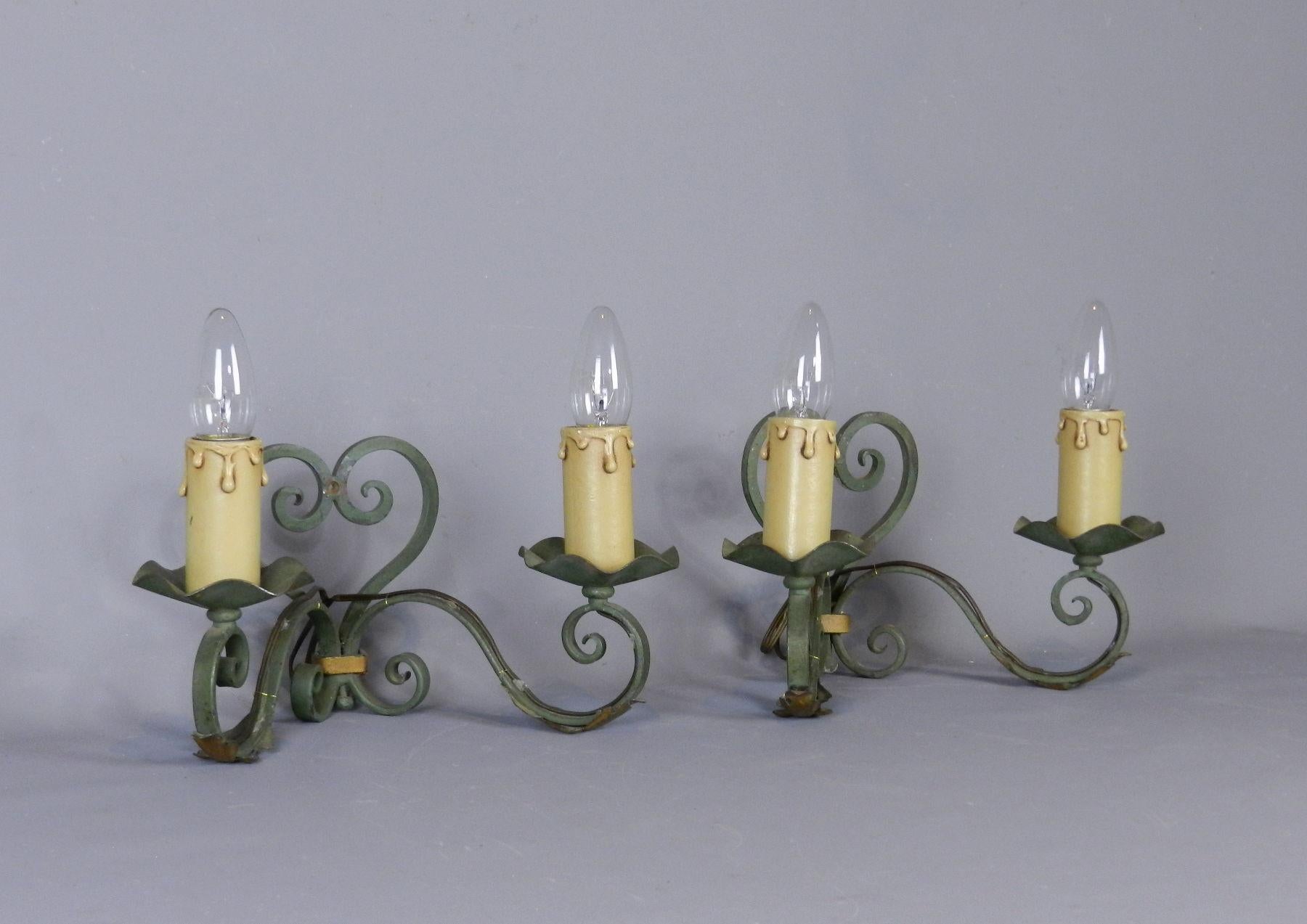A Pretty Pair of twin-armed Wall Sconces made of hand-forged steel and tole. Painted in original faded green with foliate gilt highlights and decorative heart-shaped mount.

These lights are fitted with bayonet candle light bulbs and have been