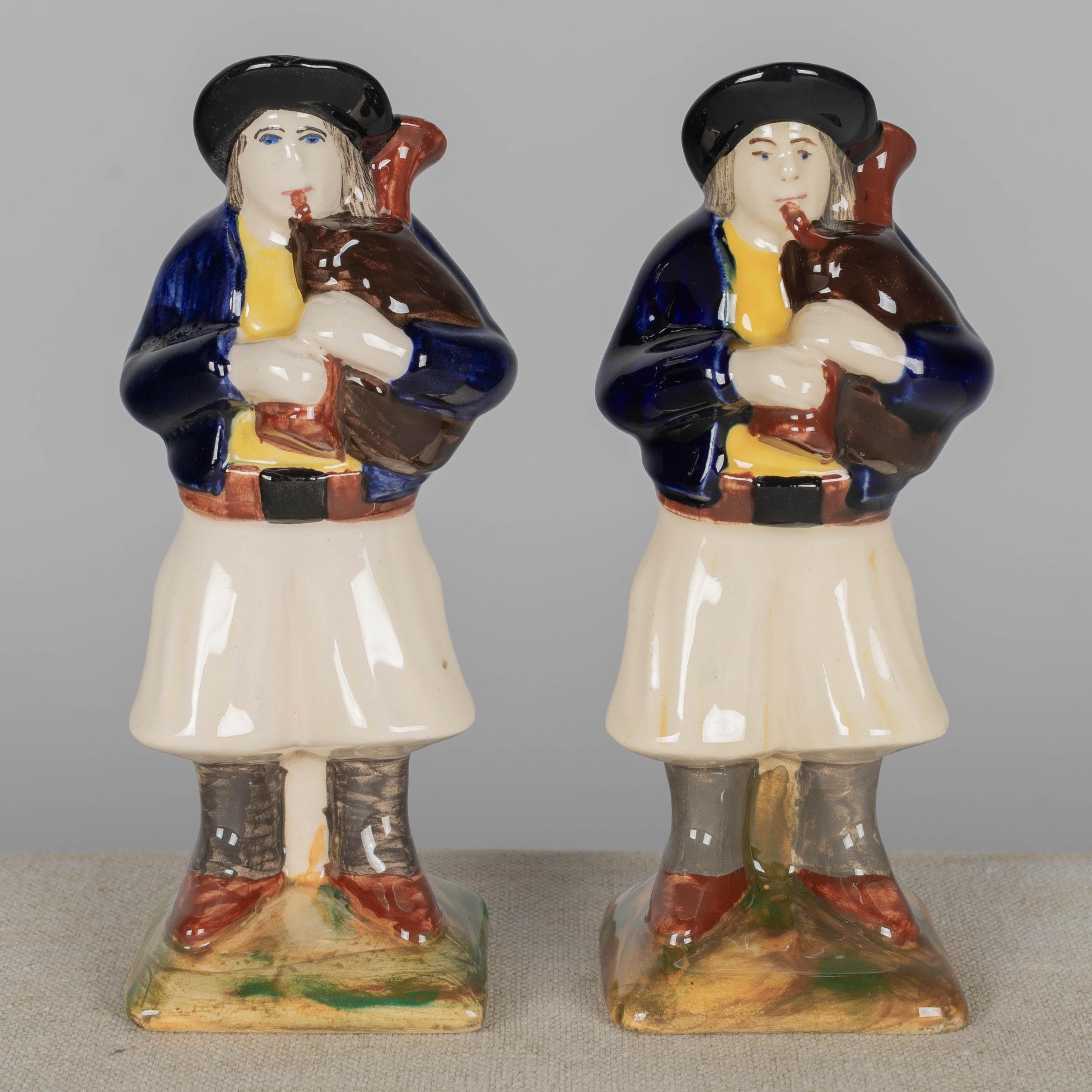 Paire de statues ou figurines en faïence de Henriot Calle, représentant des hommes jouant de la cornemuse bretonne traditionnelle appelée biniou. Faïence émaillée polychrome, peinte à la main en bleu, jaune, brun, noir et vert. Marqué sur le fond :