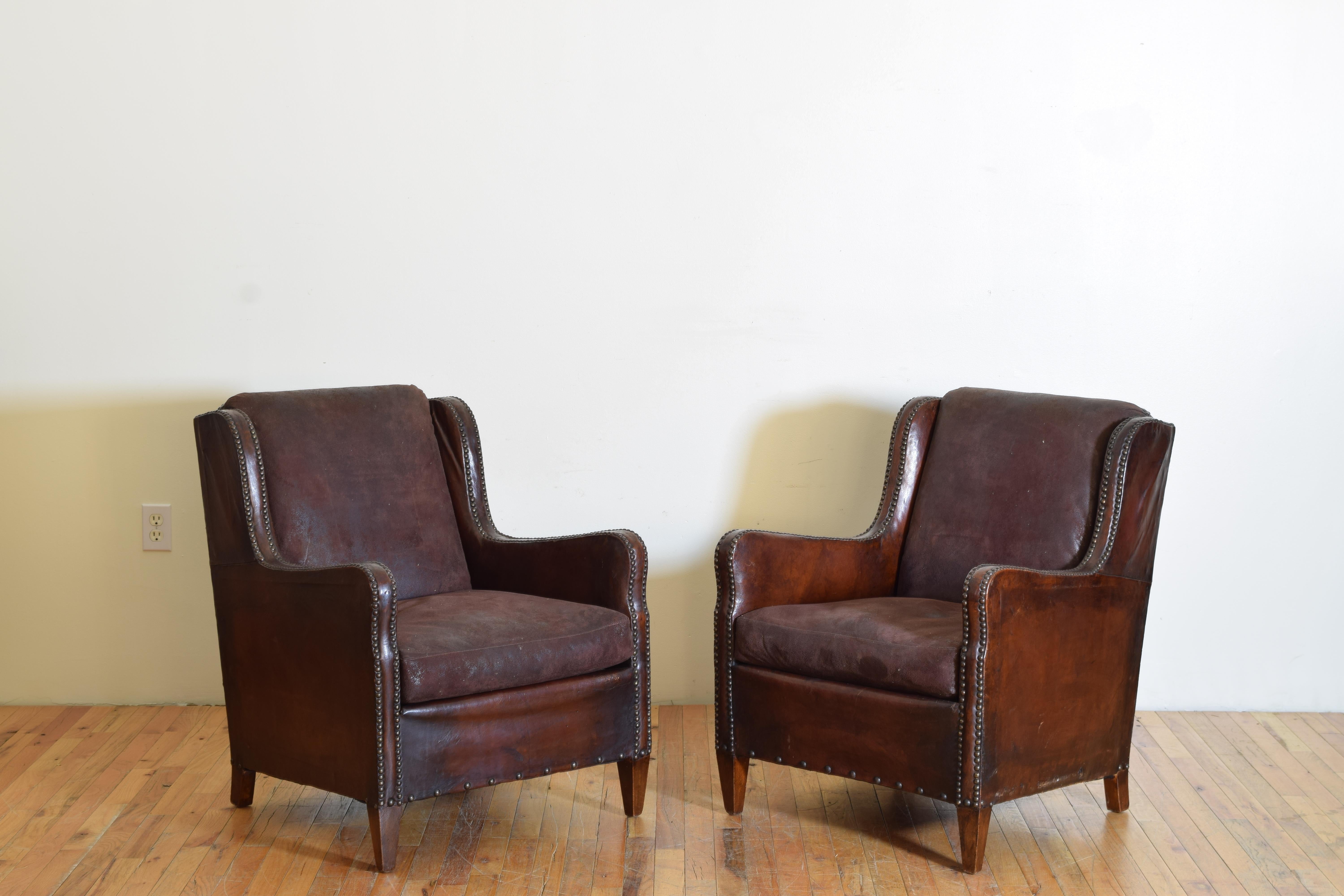 Upholstered in leather with patinated brass nailhead trim these handsome and beautifully shaped chairs feature shaped sides with slightly ascending arms, the seat and backrests upholstered in complimentary suede, raised on square tapering walnut legs