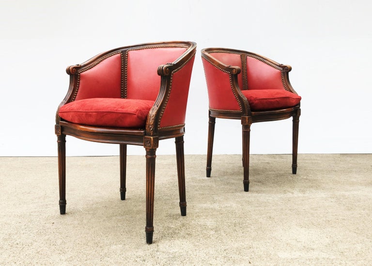 Quite an attractive pair of 19th century French Louis XVI style barrel back neoclassical armchairs. The carved frames with rich wood tone is complementary to the worn tacked pinkish red colored leather, finished with nailhead trim. It also features