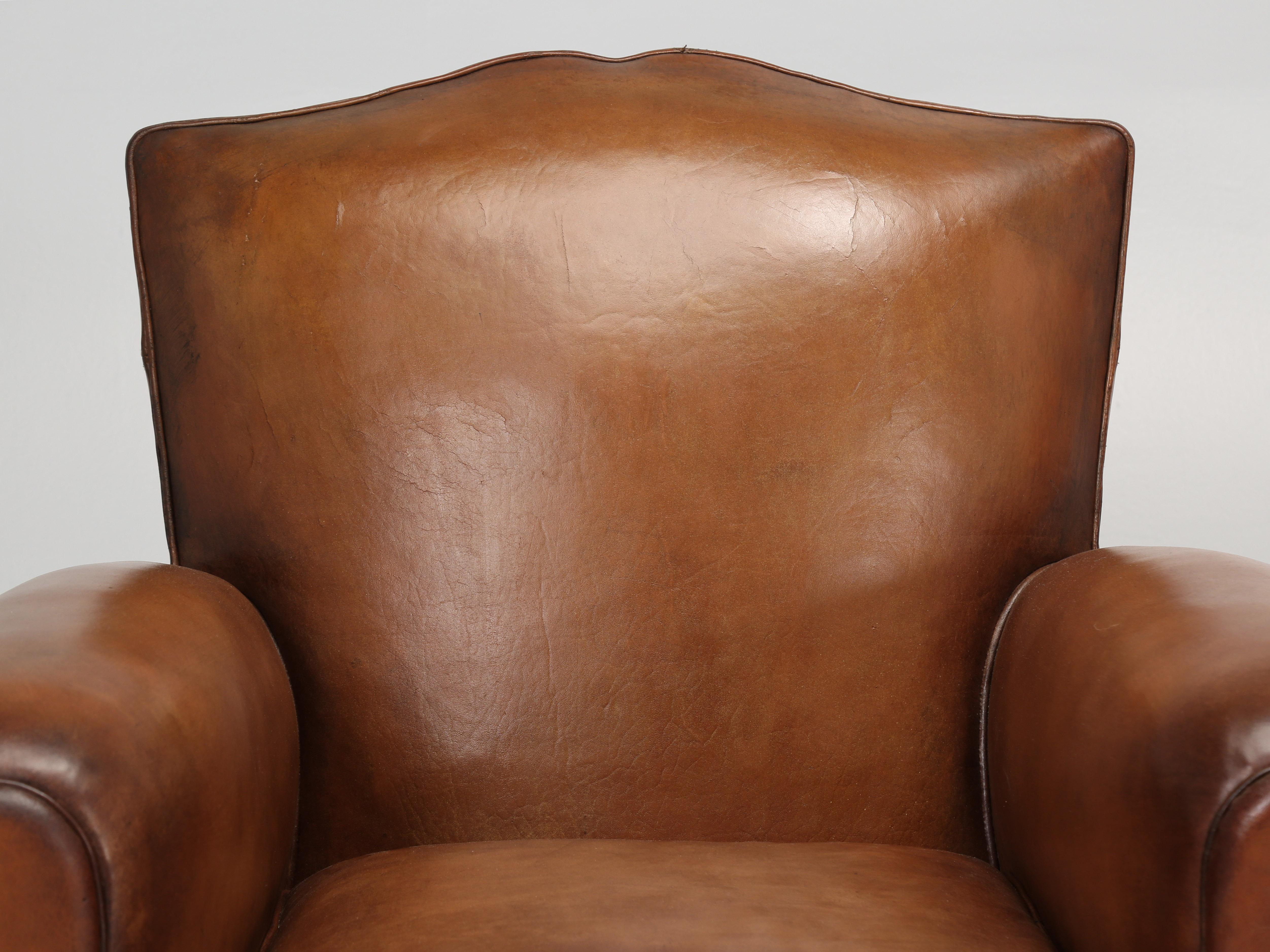 Authentic Moustache Style pair of French leather club chairs, that remain mostly in their original leather. Virtually 90% of all the club chair restorations going through our upholstery department, will require at least one or two areas where the